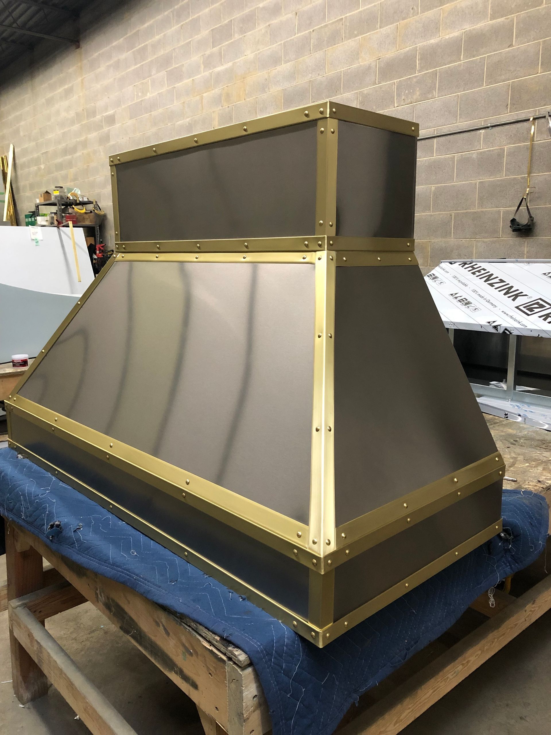 Large custom gray and gold metal box or vent housing on a blue pallet in a workshop.