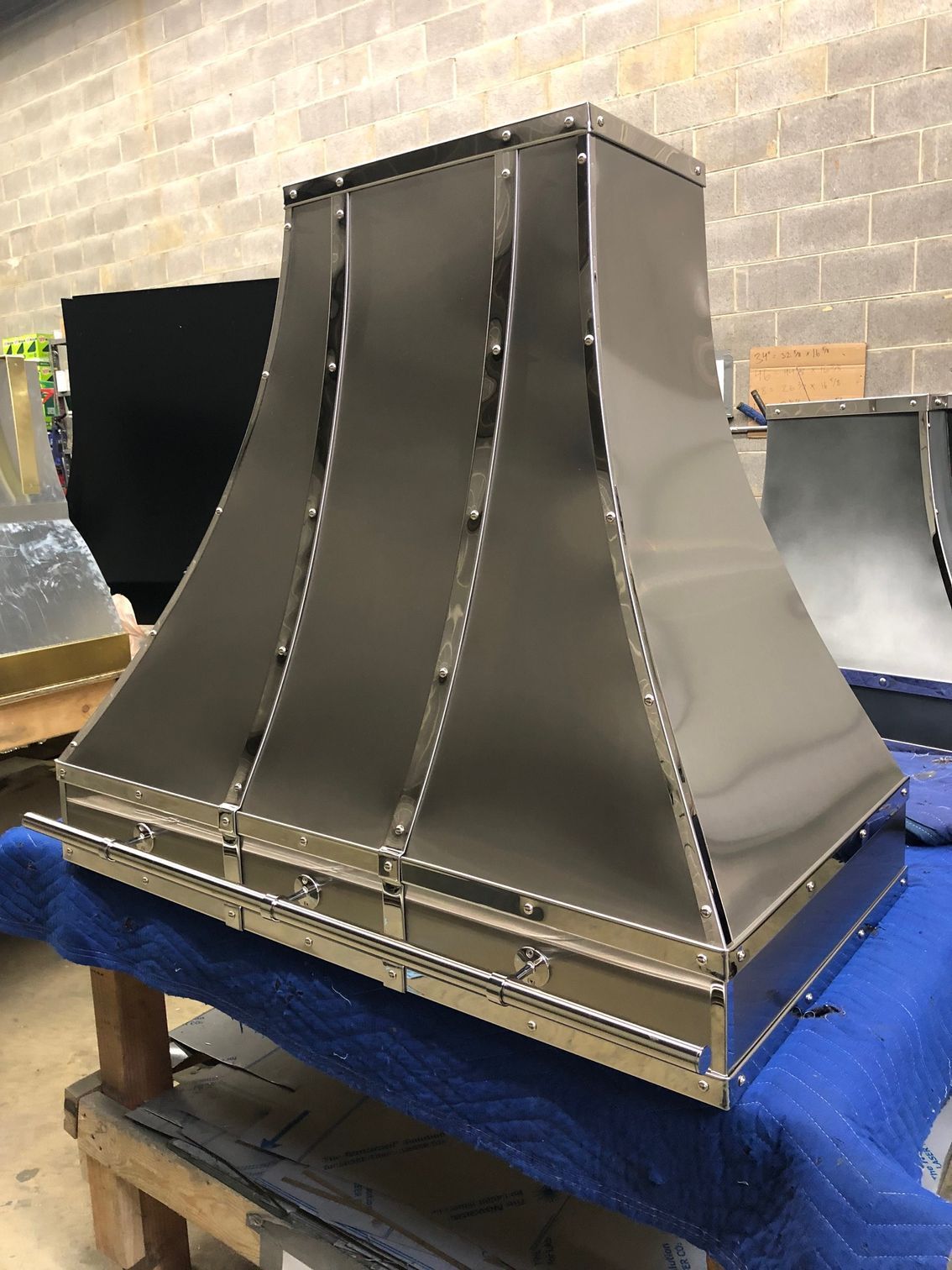Metal industrial duct or vent hood on a blue-covered workbench in a workshop