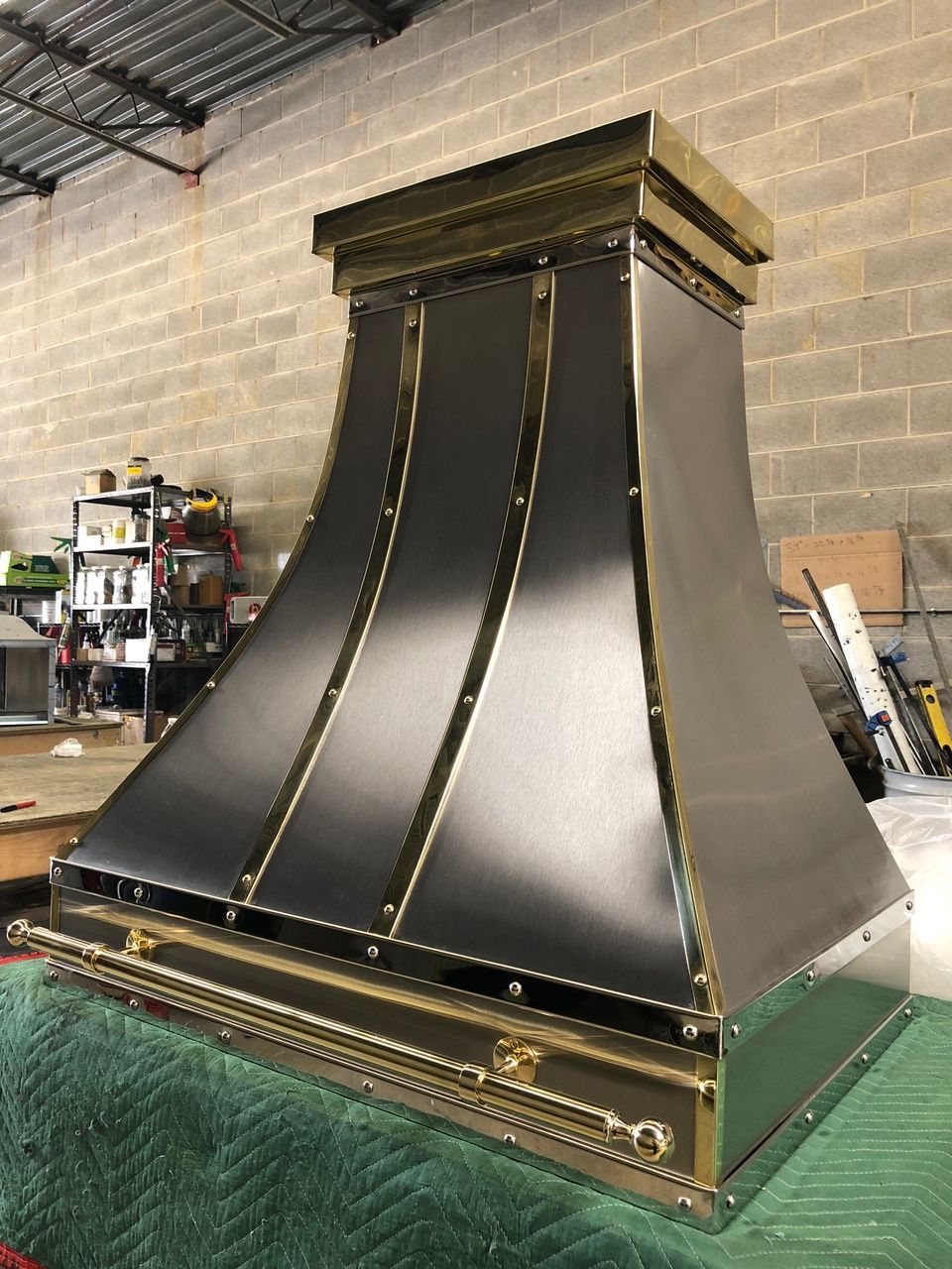 Large black-and-gold decorative metal hood or chimney cover in a workshop setting