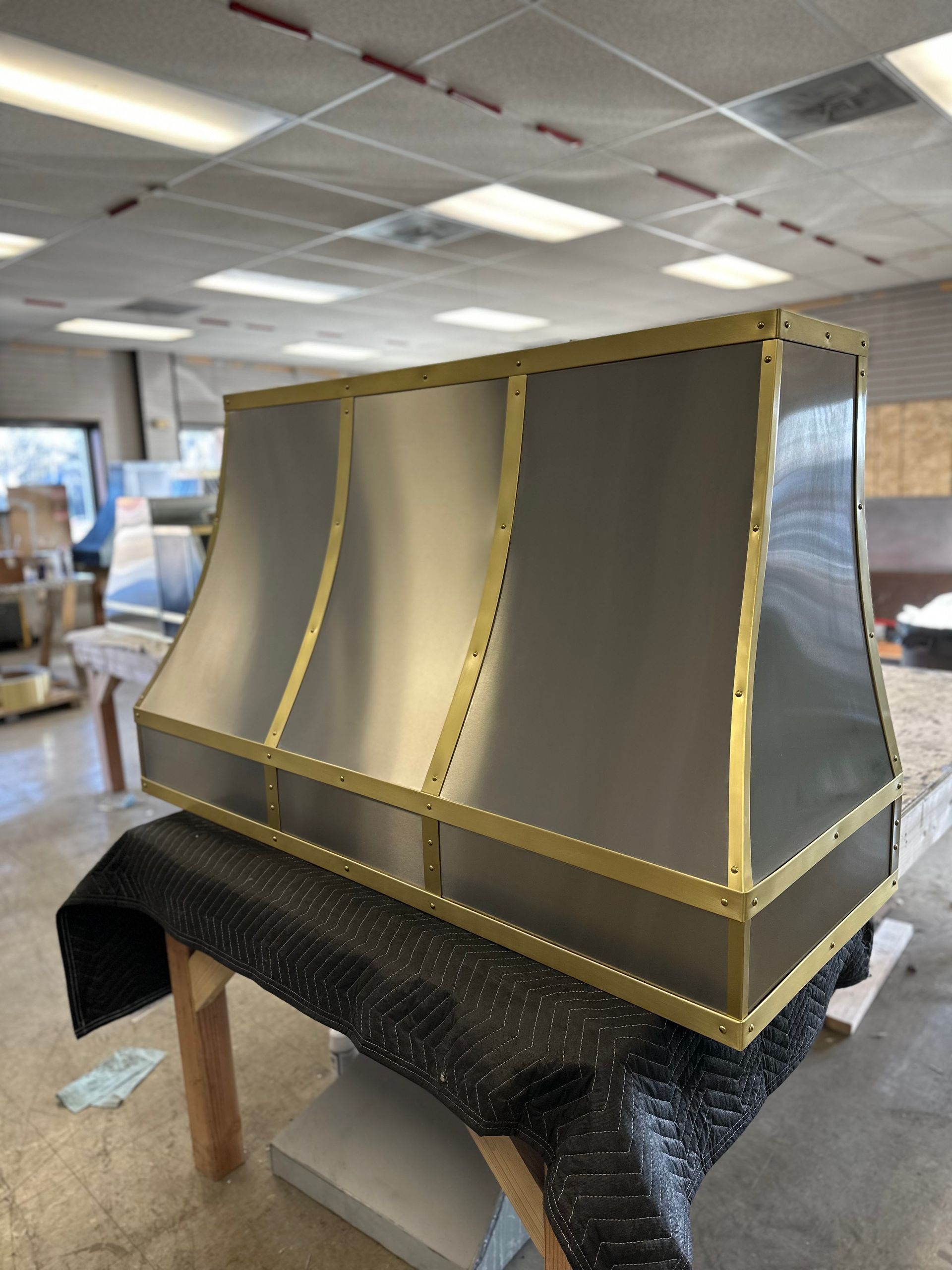 Large gold-framed metal structure on a work table in a workshop, with white ceiling tiles in the background