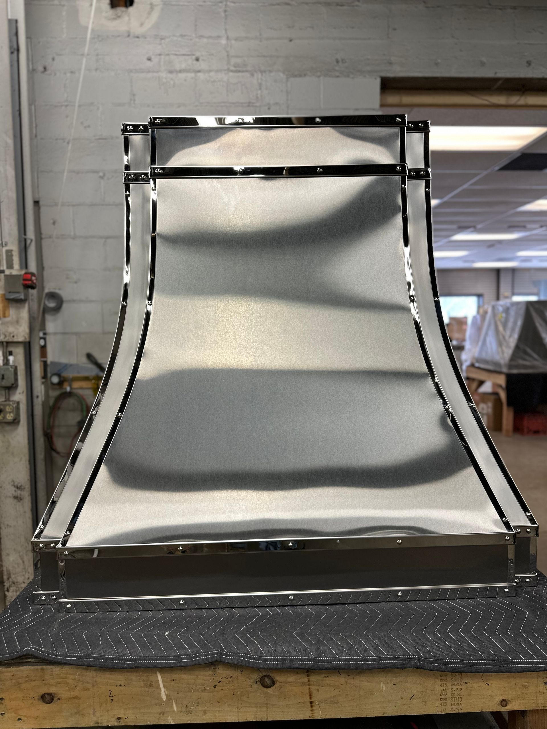 Metal duct or vent section on a workbench in a workshop, with a curved silver front and black edges