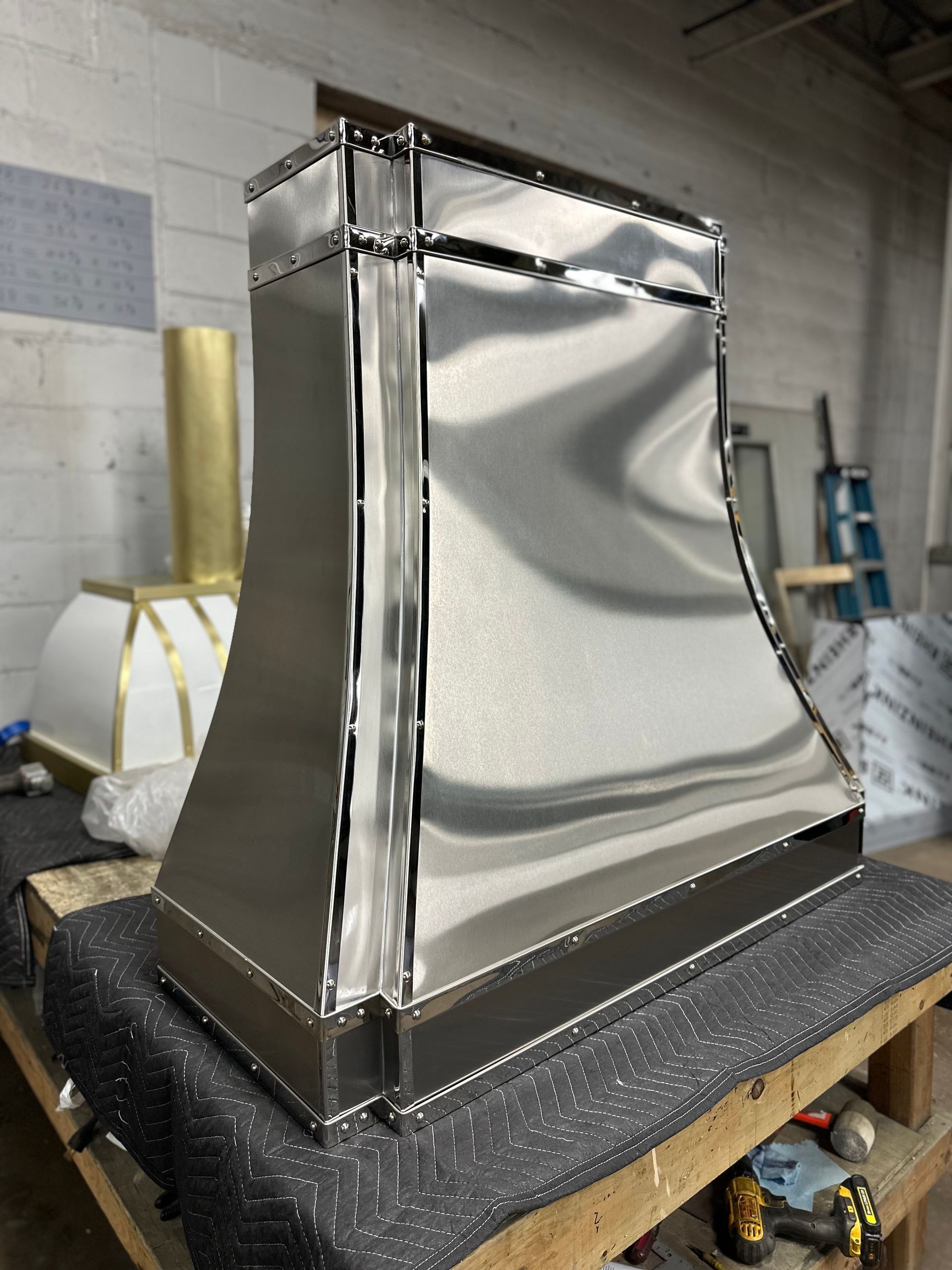 Shiny metal HVAC duct section on a workshop table, with taped seams and a curved front panel