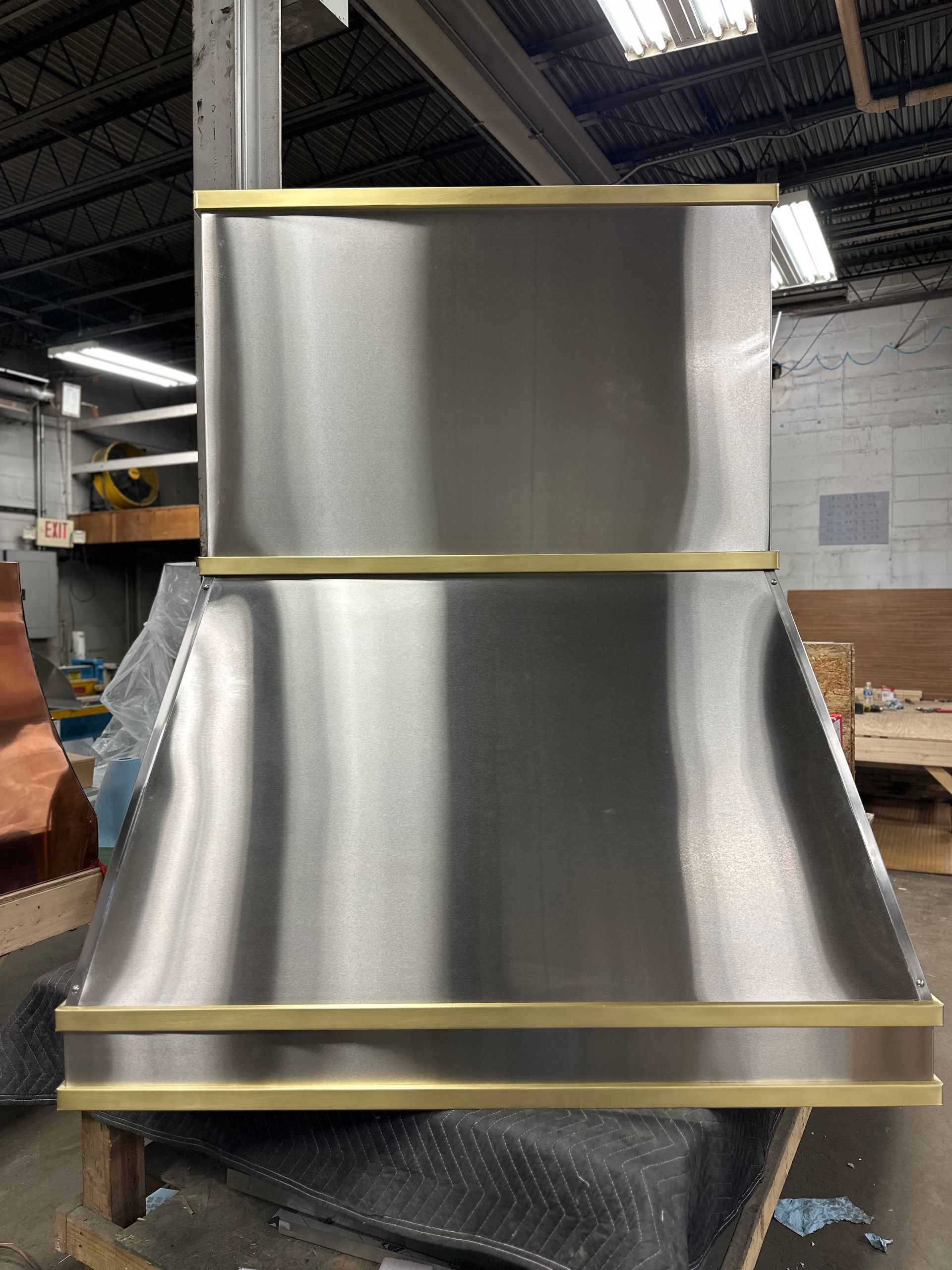 Metal HVAC duct section in a warehouse, with shiny silver panels and yellow trim bands.