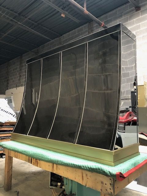Large black mesh panel with white seams mounted on a green-lit worktable in an industrial workshop.
