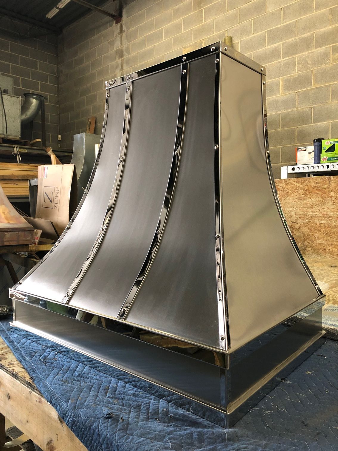 Large metallic duct or exhaust hood prototype with curved silver panels in a workshop.