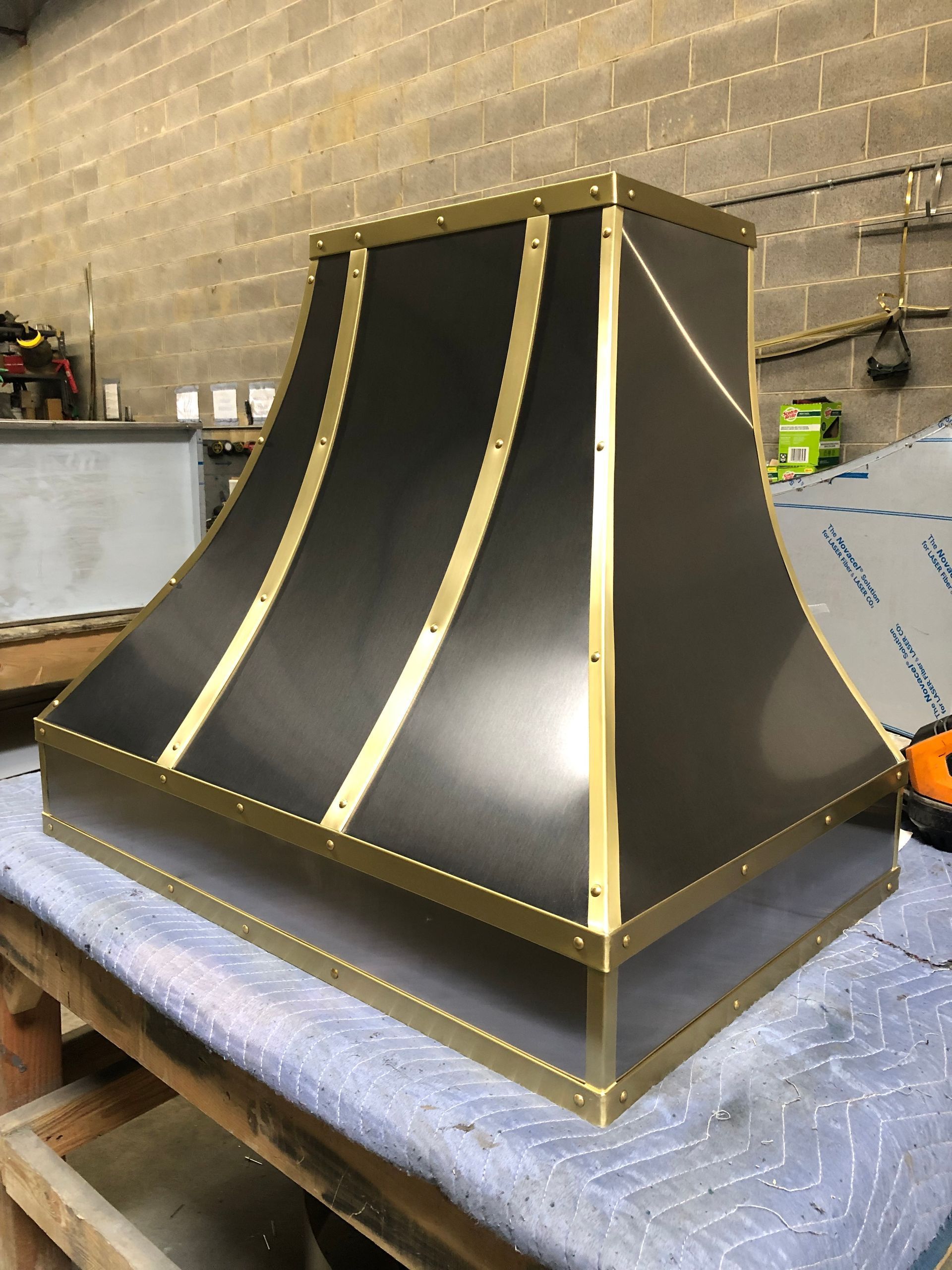 Black metal hood with gold trim on a workbench in a workshop