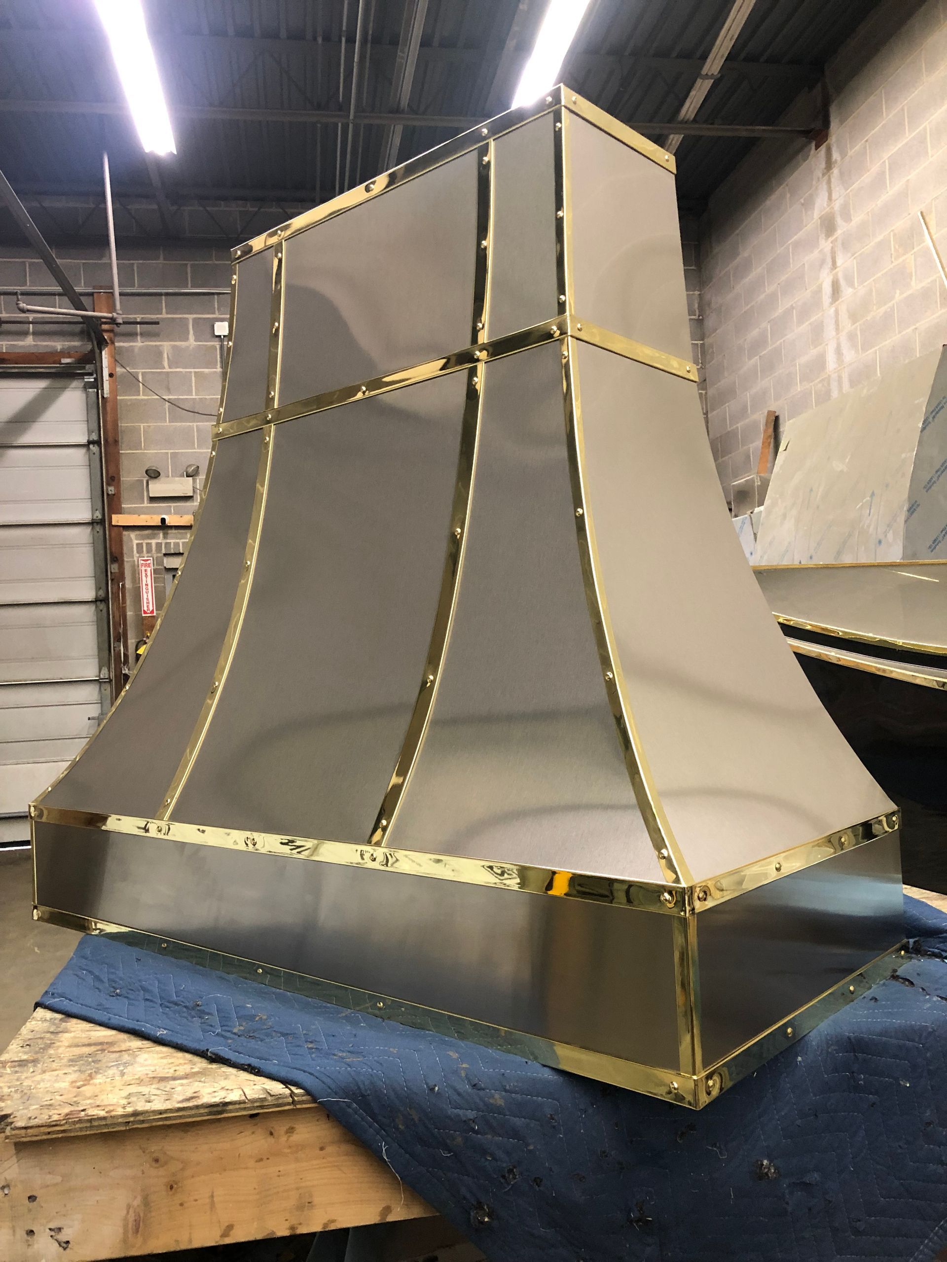 Large gray duct or hood prototype with gold tape seams, sitting on a blue-covered workbench in a workshop.