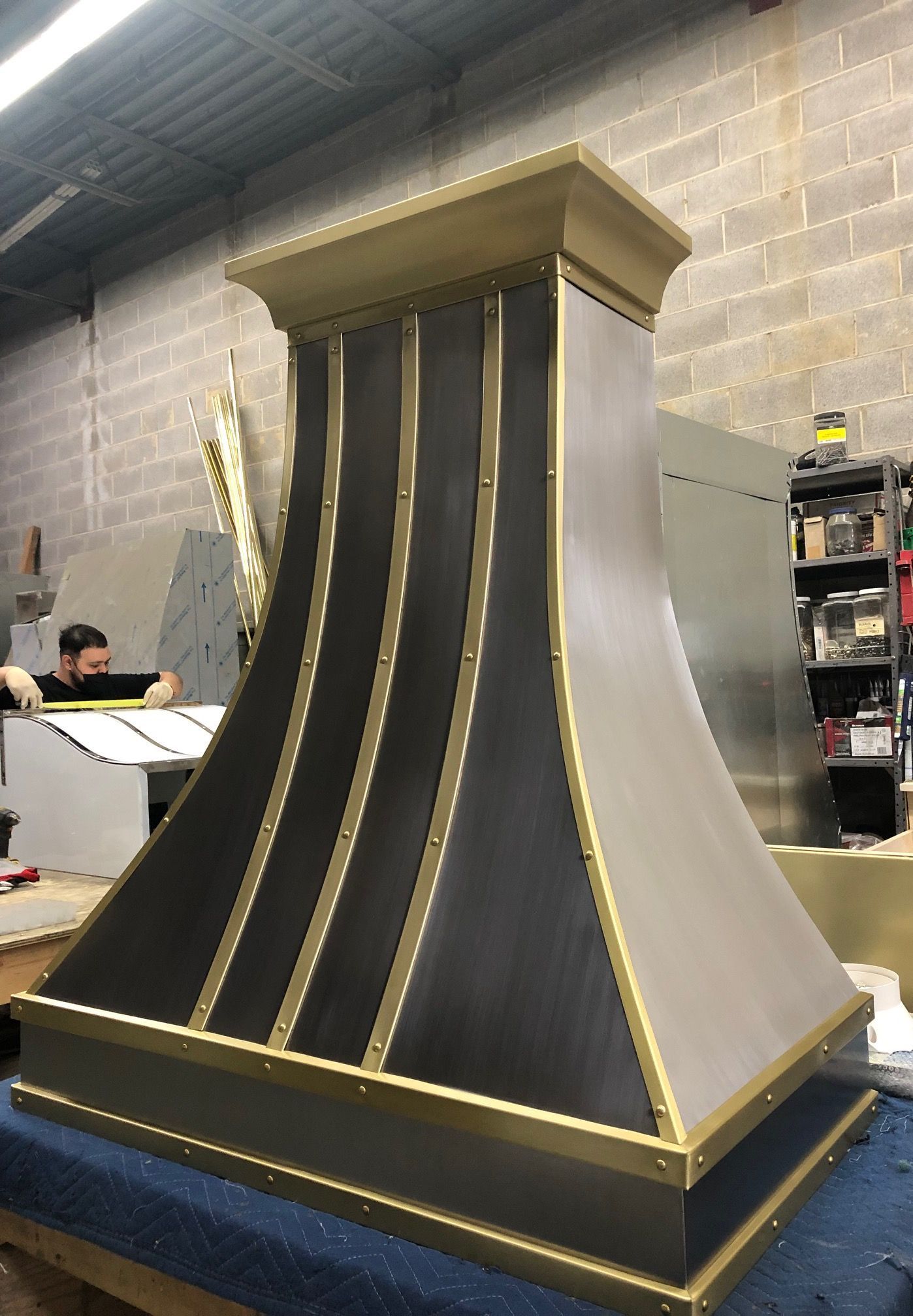 Gold-and-black decorative vent or hood prototype in a workshop, with curved metal sides and a square top cap