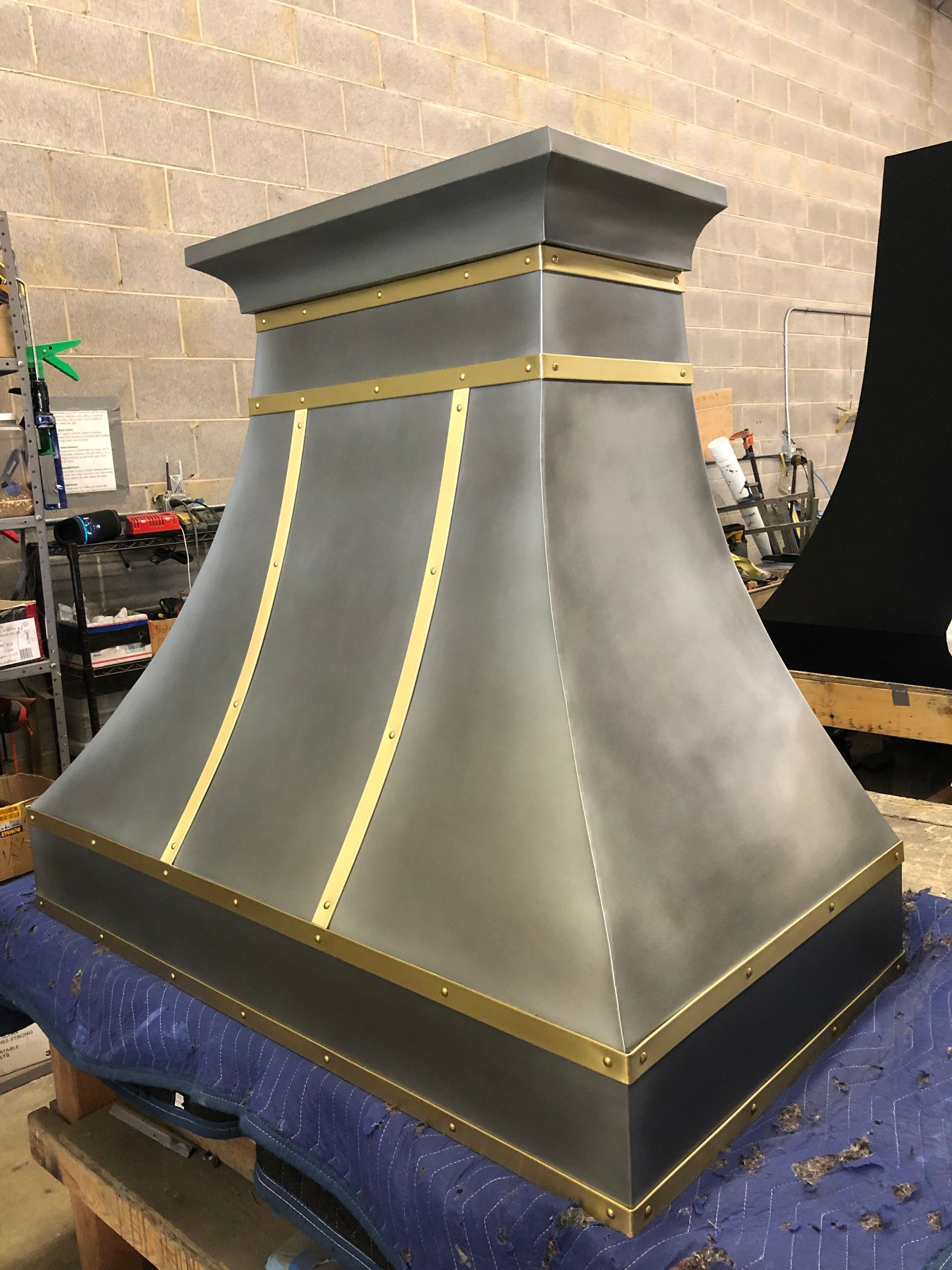 Large gray metal chimney cap with gold trim on a workbench in a workshop