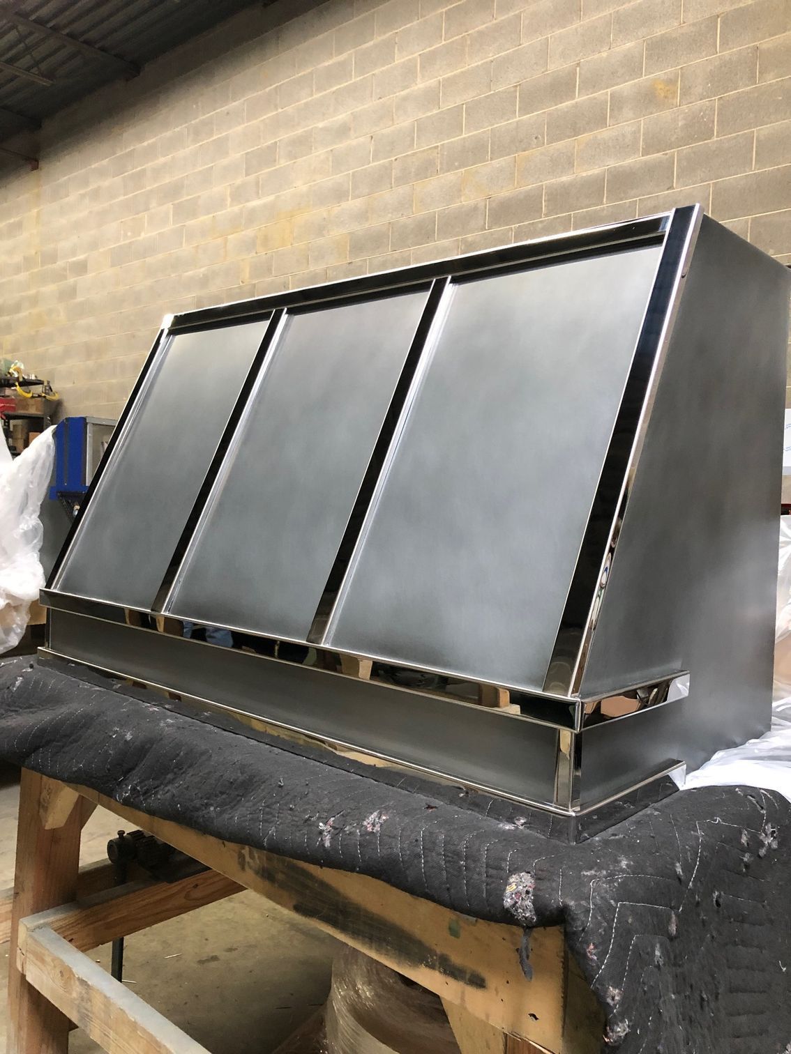 Black slanted metal panel assembly on a workbench in a workshop, with brick wall background