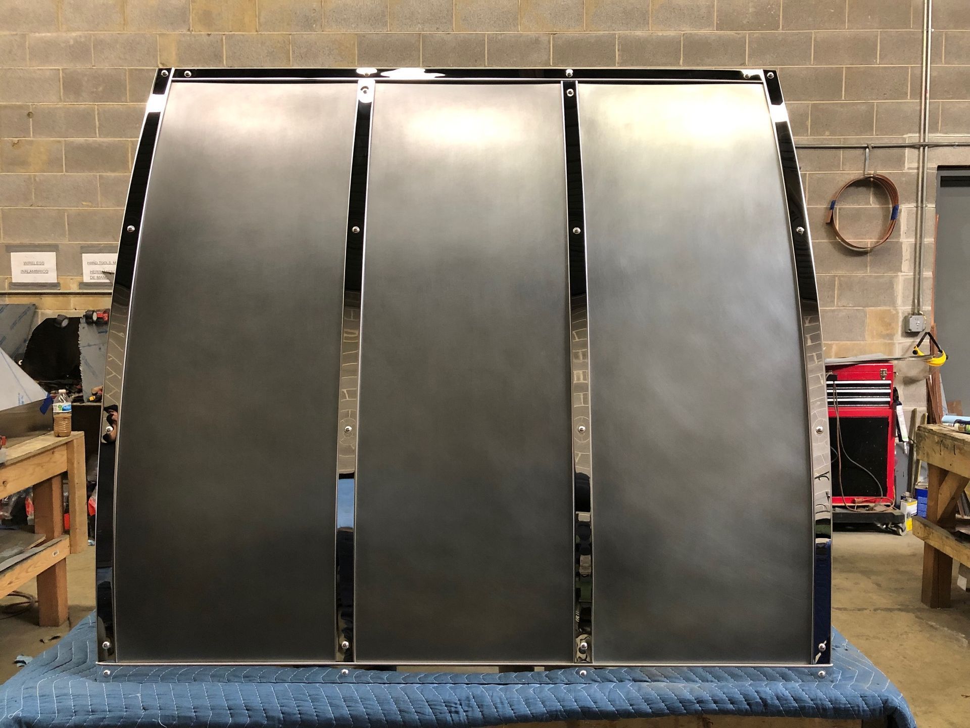 Three large curved metal panels standing in a workshop on a blue pallet