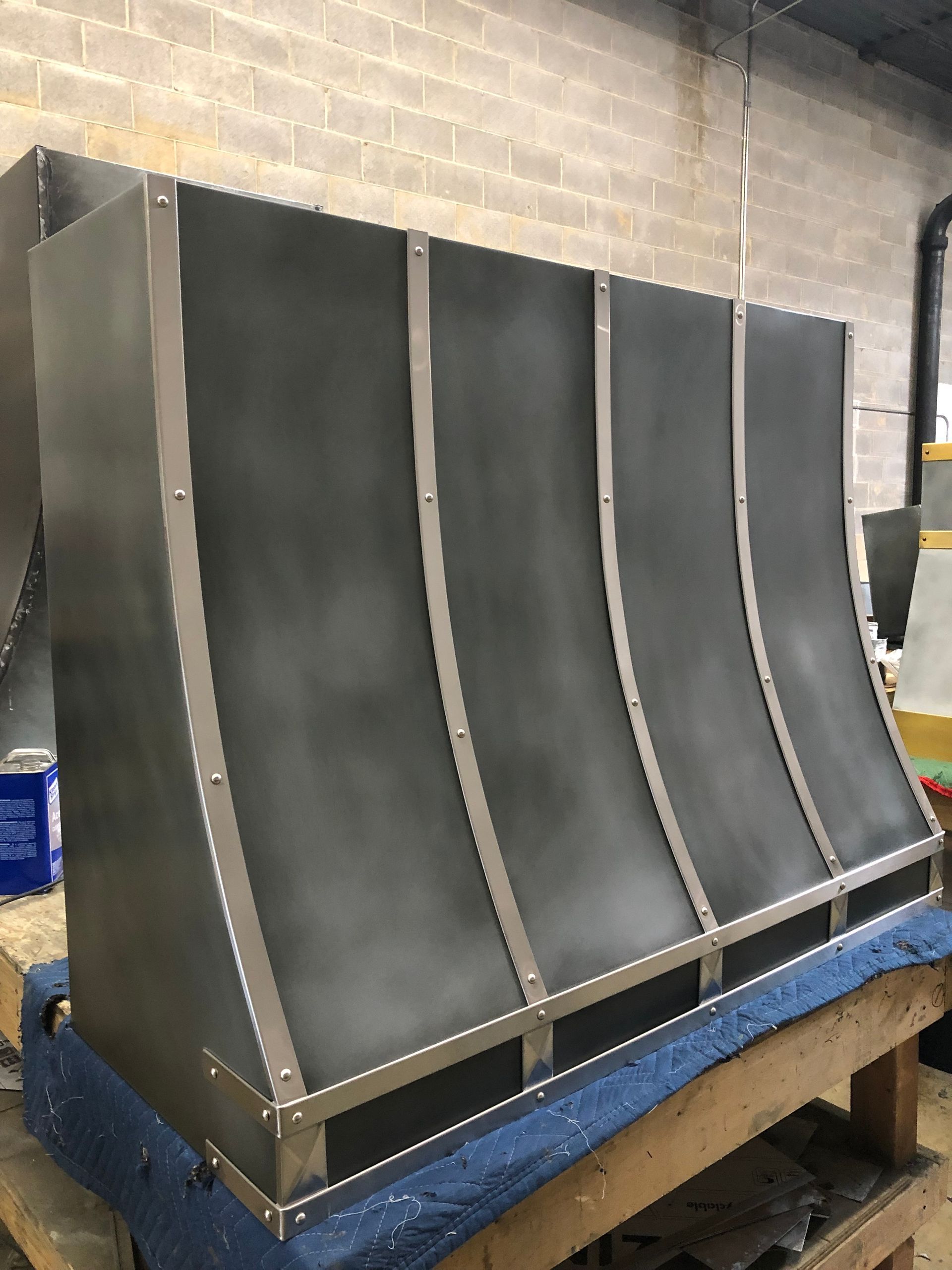 Curved black metal panels mounted on a blue workbench in a workshop