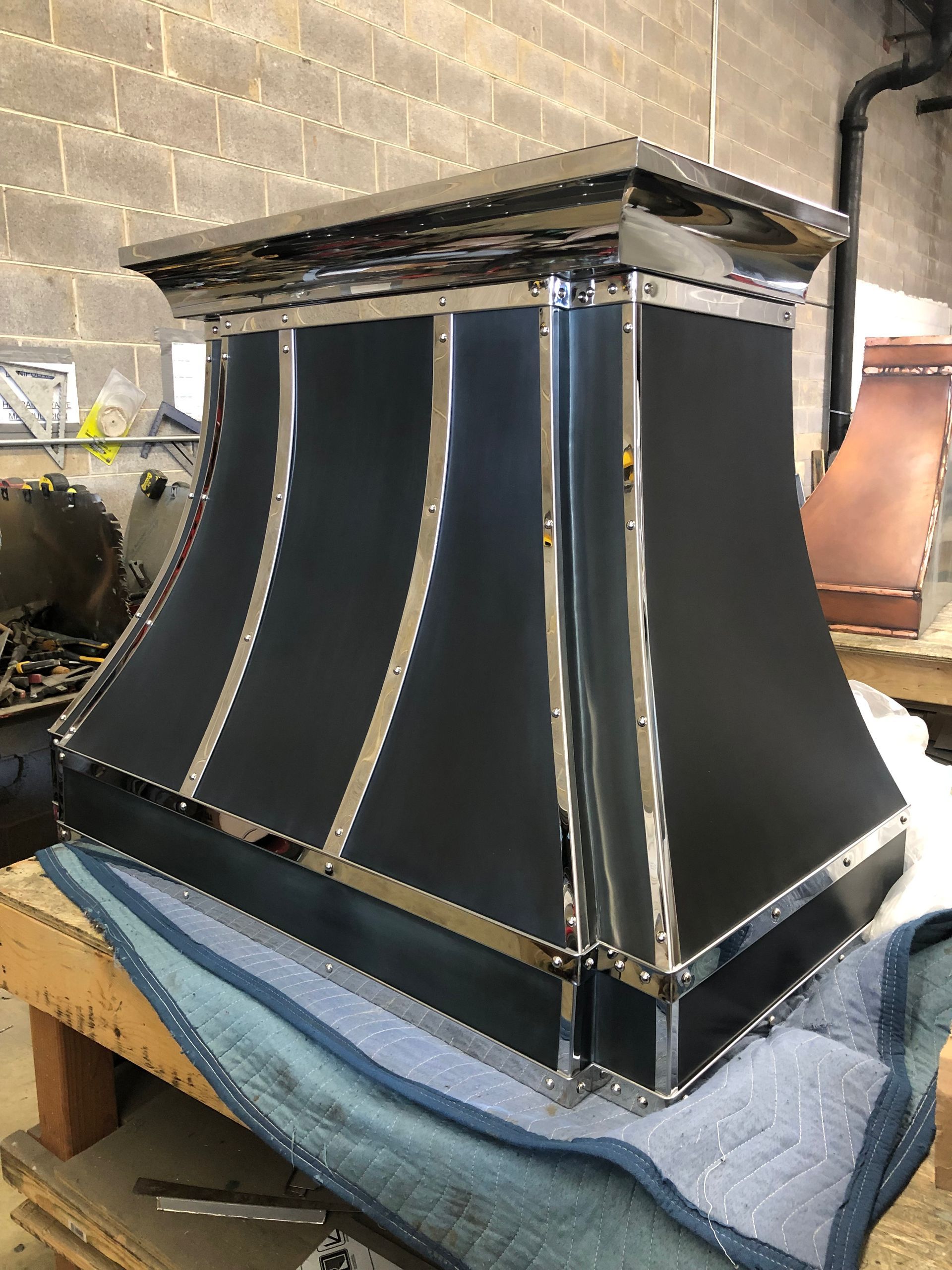 Black metal vent hood with silver trim sitting on a workbench in a workshop