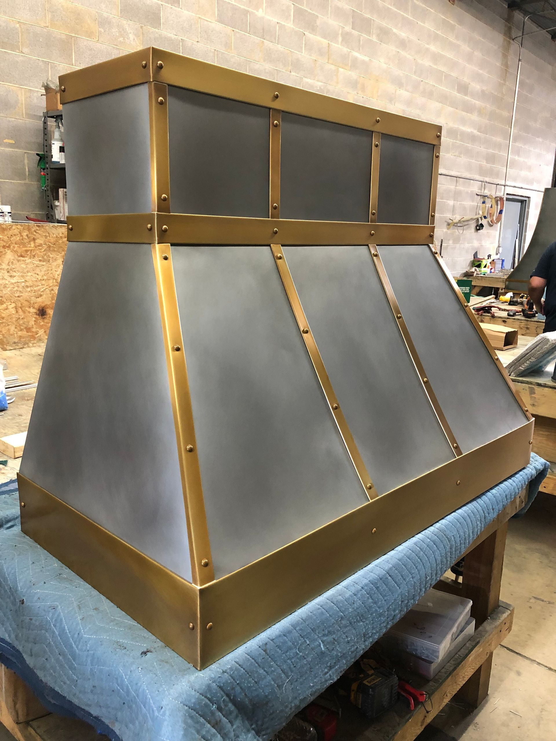Metal vent hood prototype with gray panels and gold trim on a workbench in a workshop