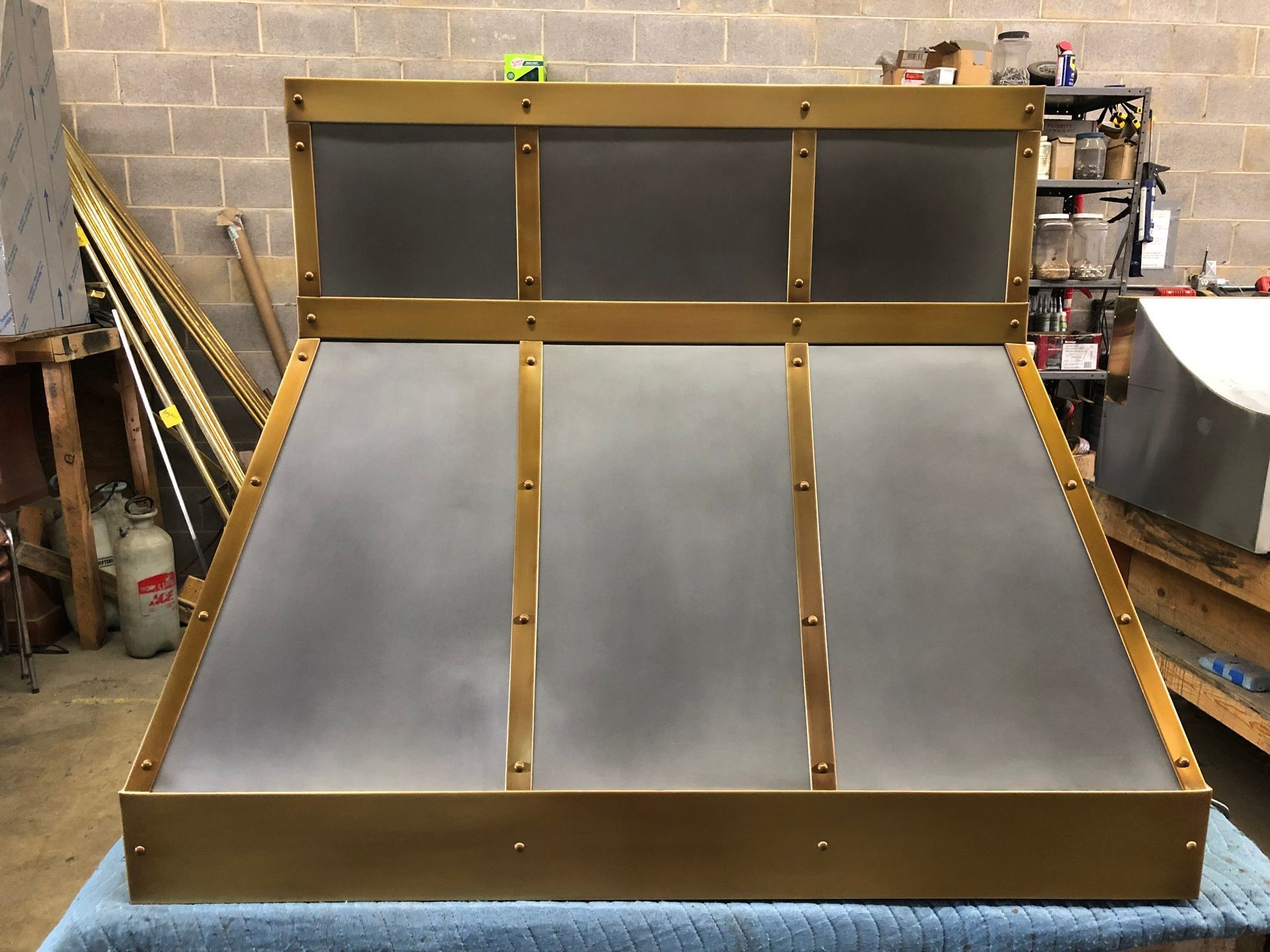 Metal skate ramp with gray riding surface and brown frame in a workshop.