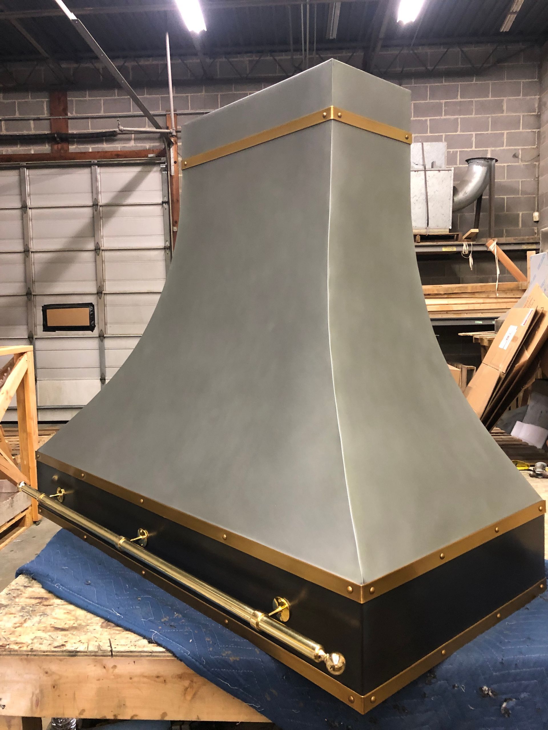 Large gray industrial hood with black base, sitting on a wooden pallet in a workshop.