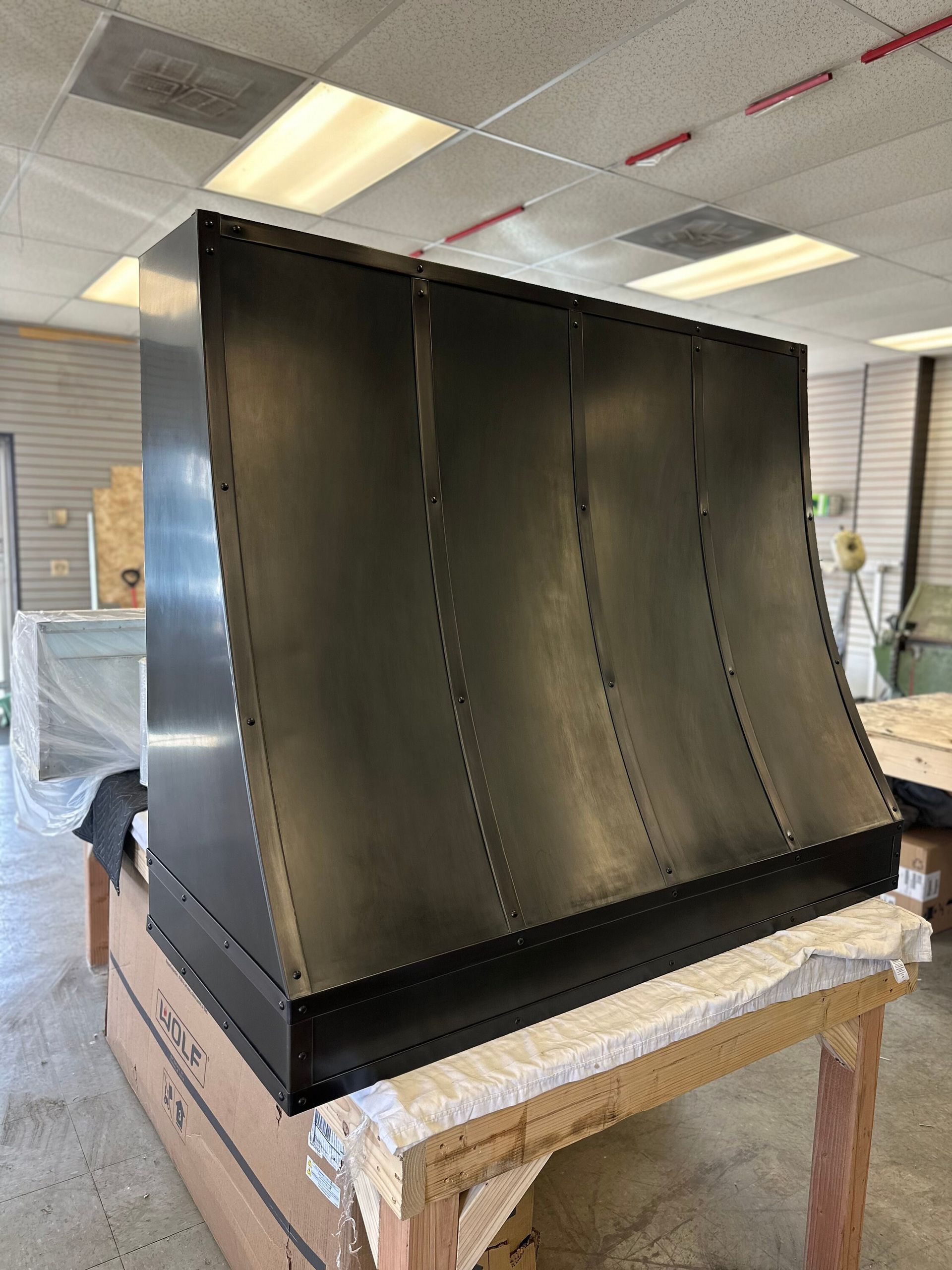 Large black curved metal panel on a wooden stand in a workshop or lab room