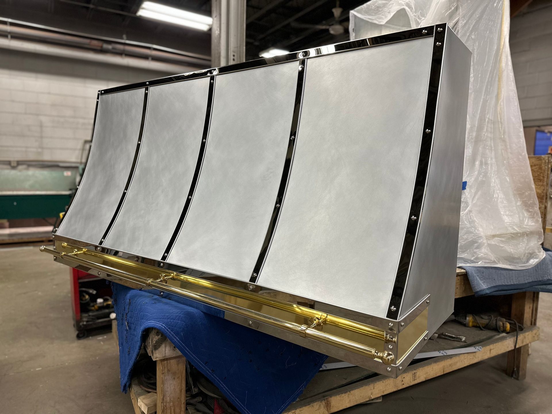 Large white panel assembly with black seams and gold base on a blue tarp in an indoor workshop