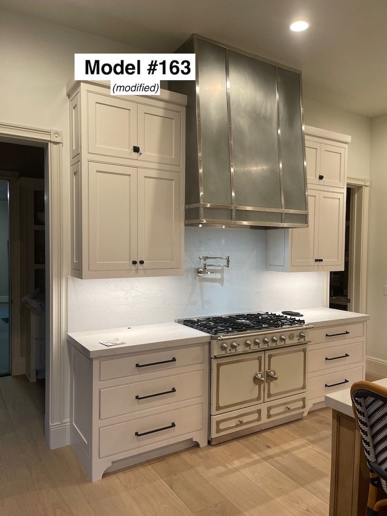Luxury white kitchen with stainless range hood, cream cabinets, and light wood floors