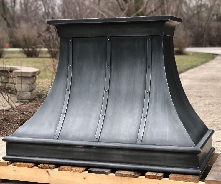 Black curved metal range hood resting on wooden pallets outdoors.