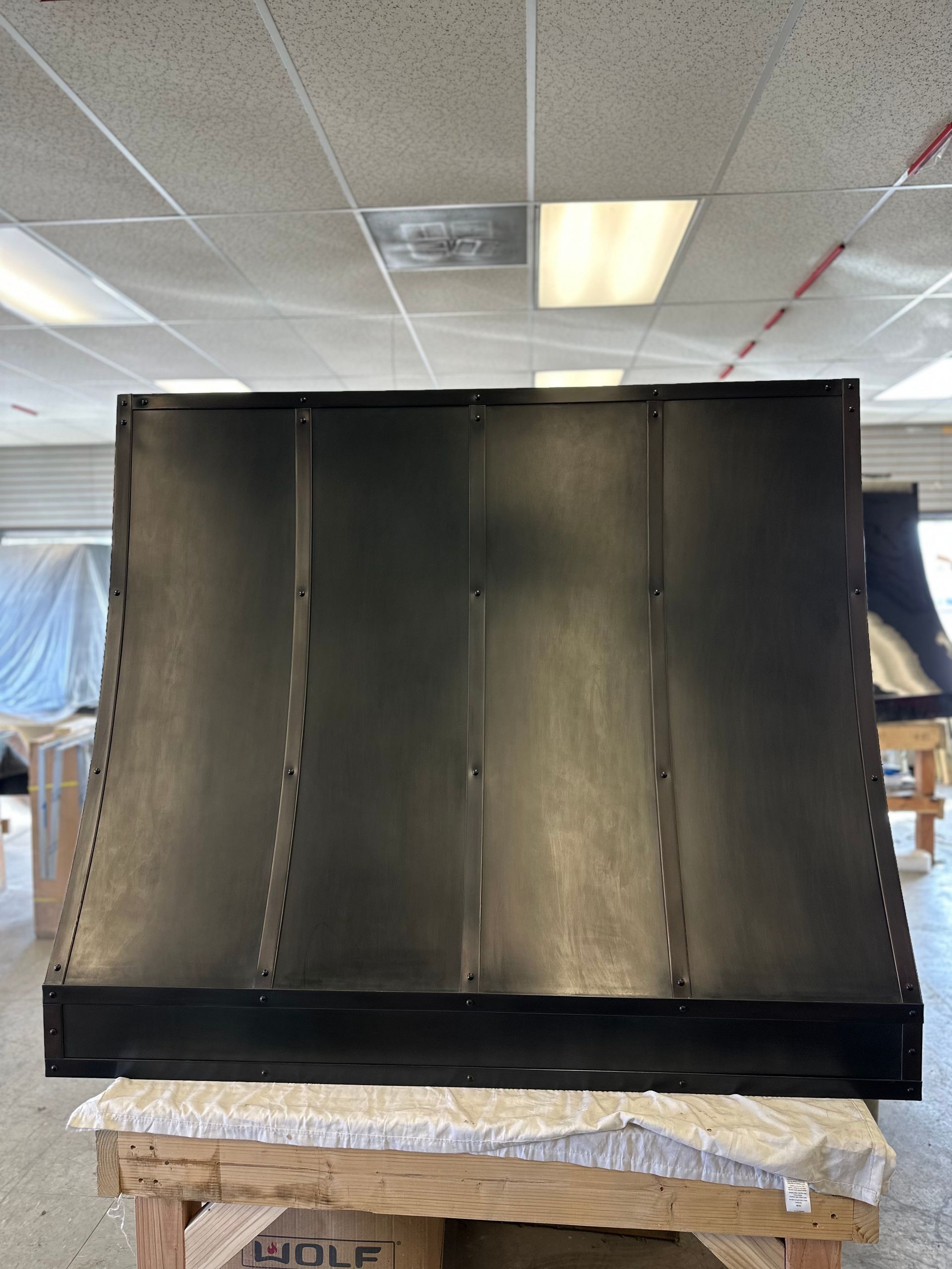 Black metal hood or duct piece on a workbench in a workshop ceiling room.
