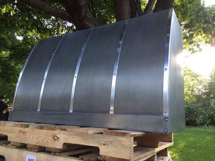 Large curved black metal panel resting on wooden pallets outdoors under trees
