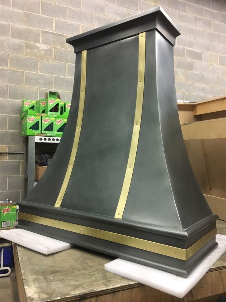 Large black and gold decorative range hood on a workbench in a workshop