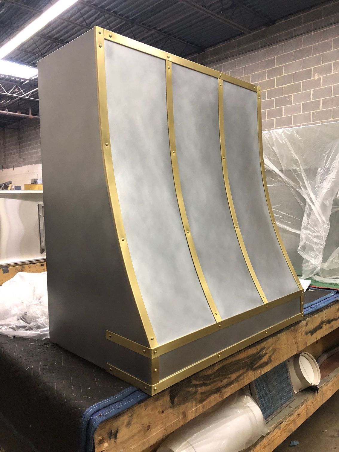 Curved metal panel with gold trim on a pallet in a warehouse workshop