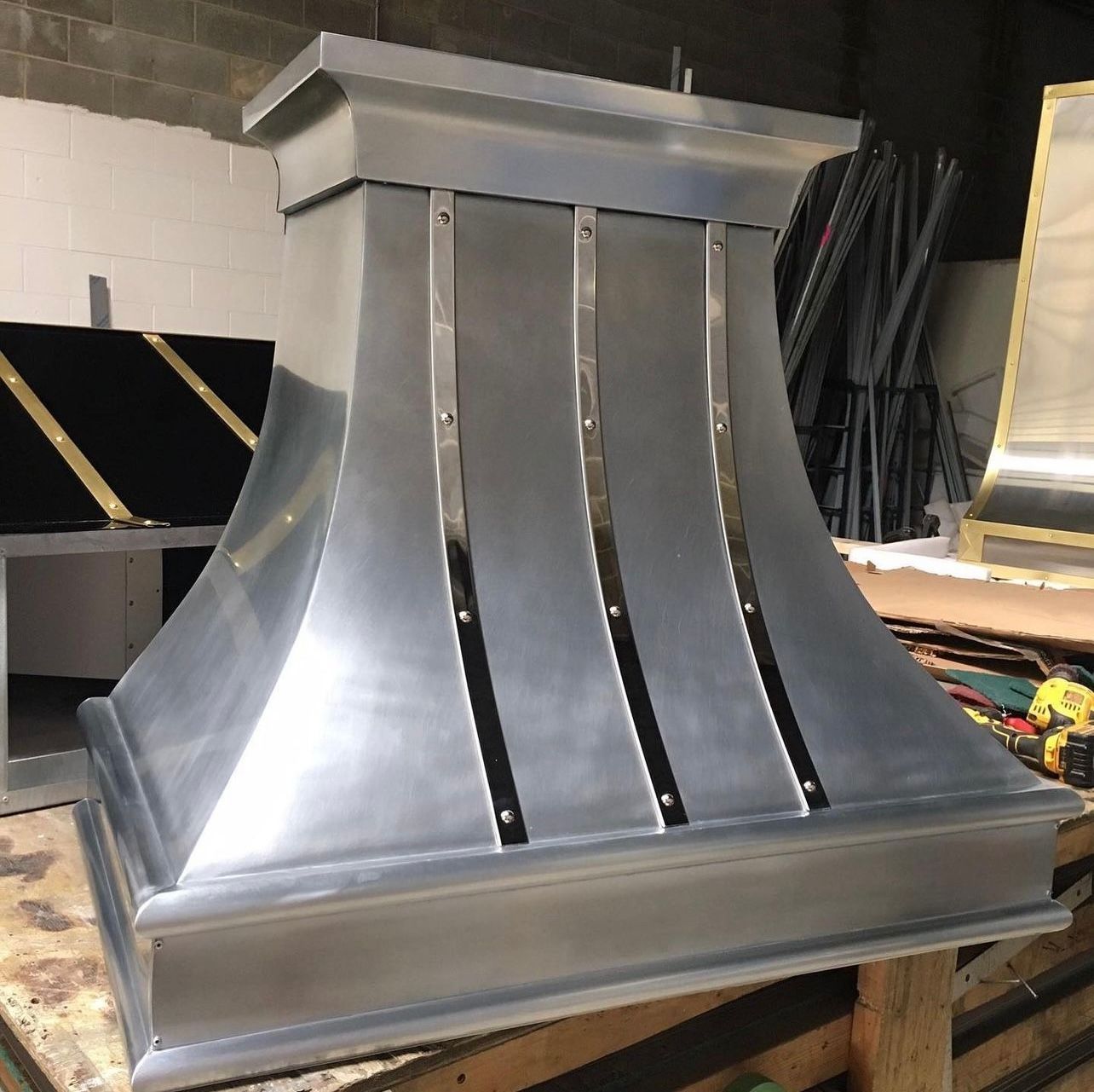 Metallic architectural vent hood with curved silver panels in a workshop.