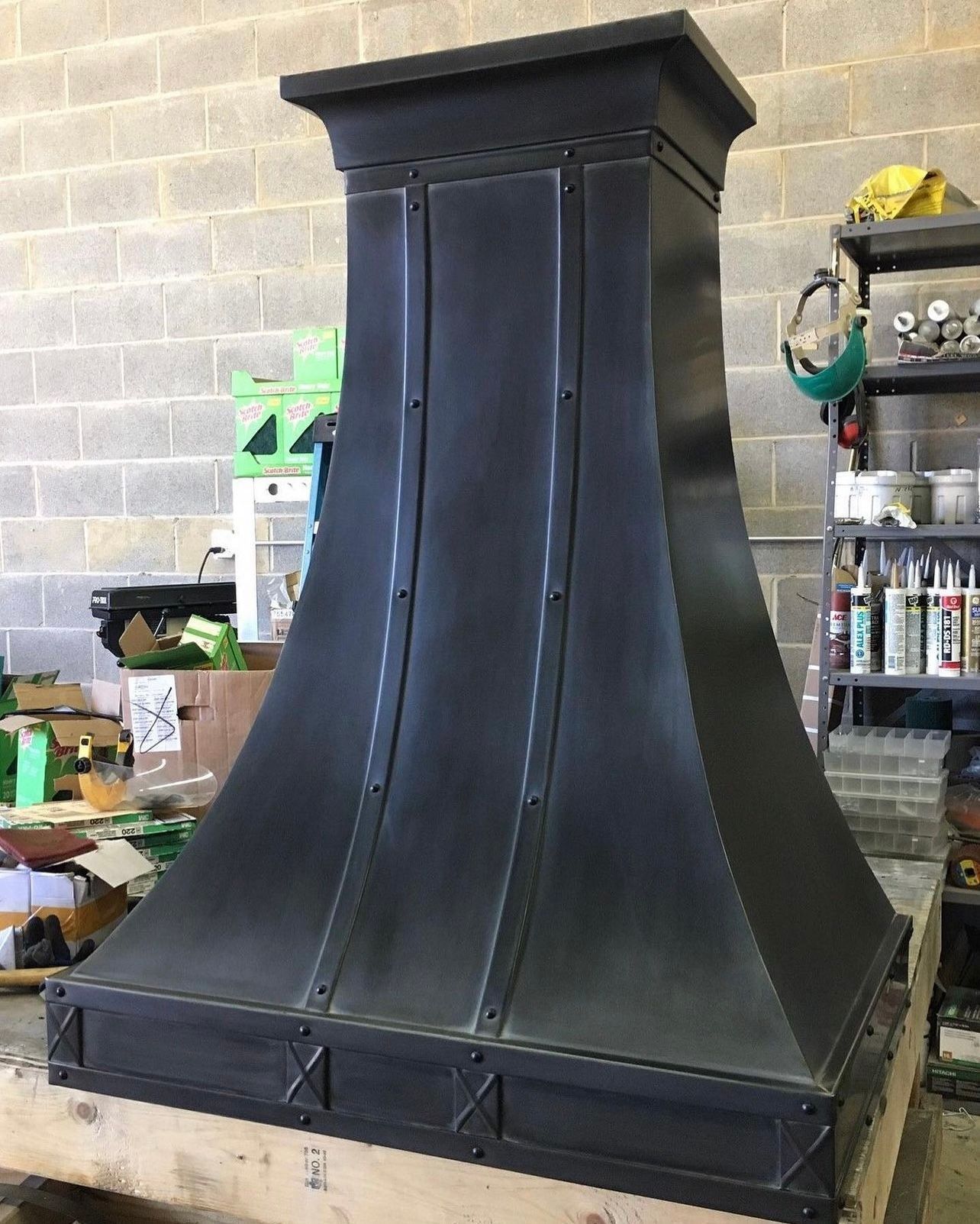 Black metal range hood or chimney cover in a workshop against a cinderblock wall