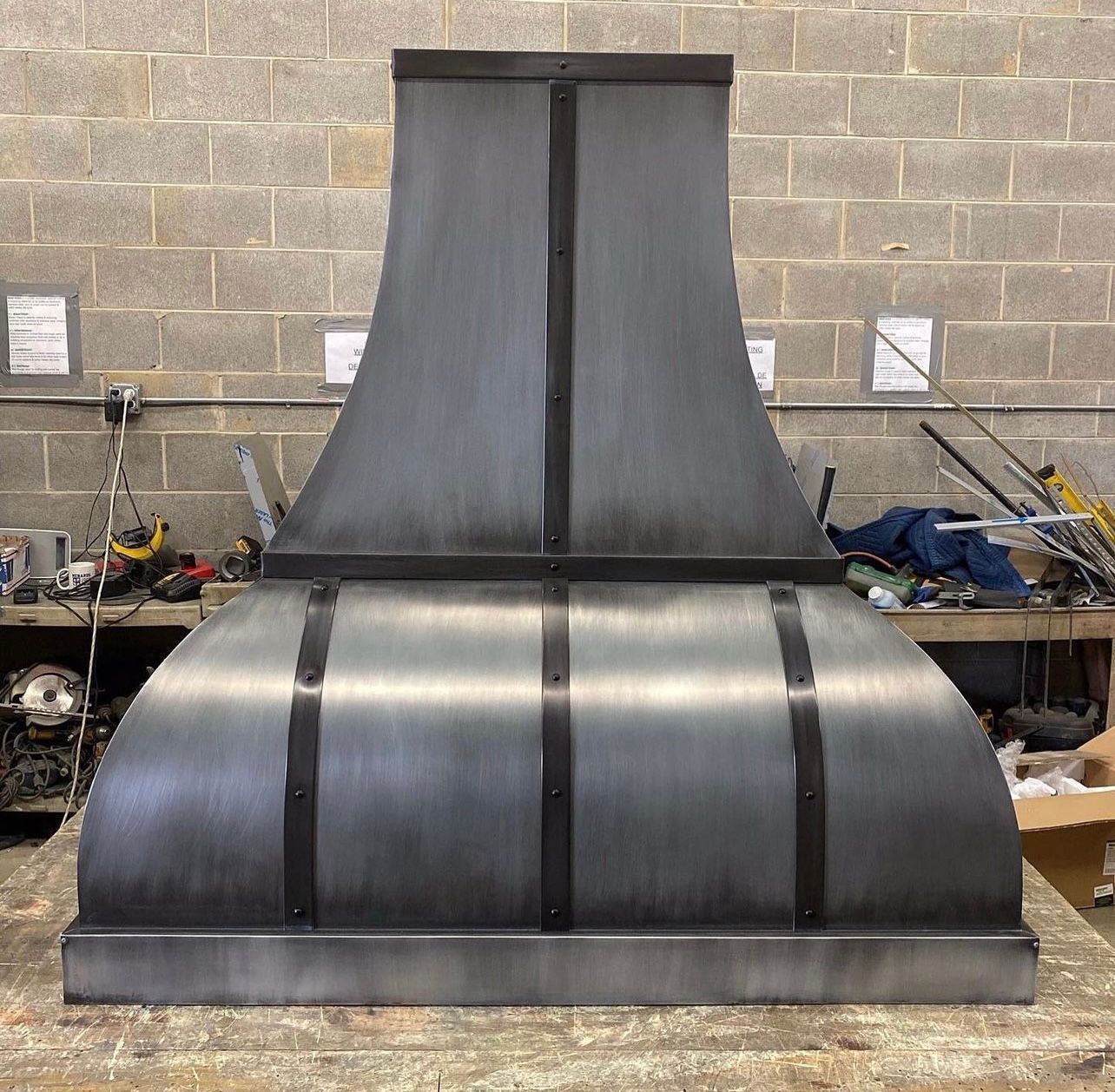 Large black industrial metal sculpture with a curved base and tall central panel in a workshop yard