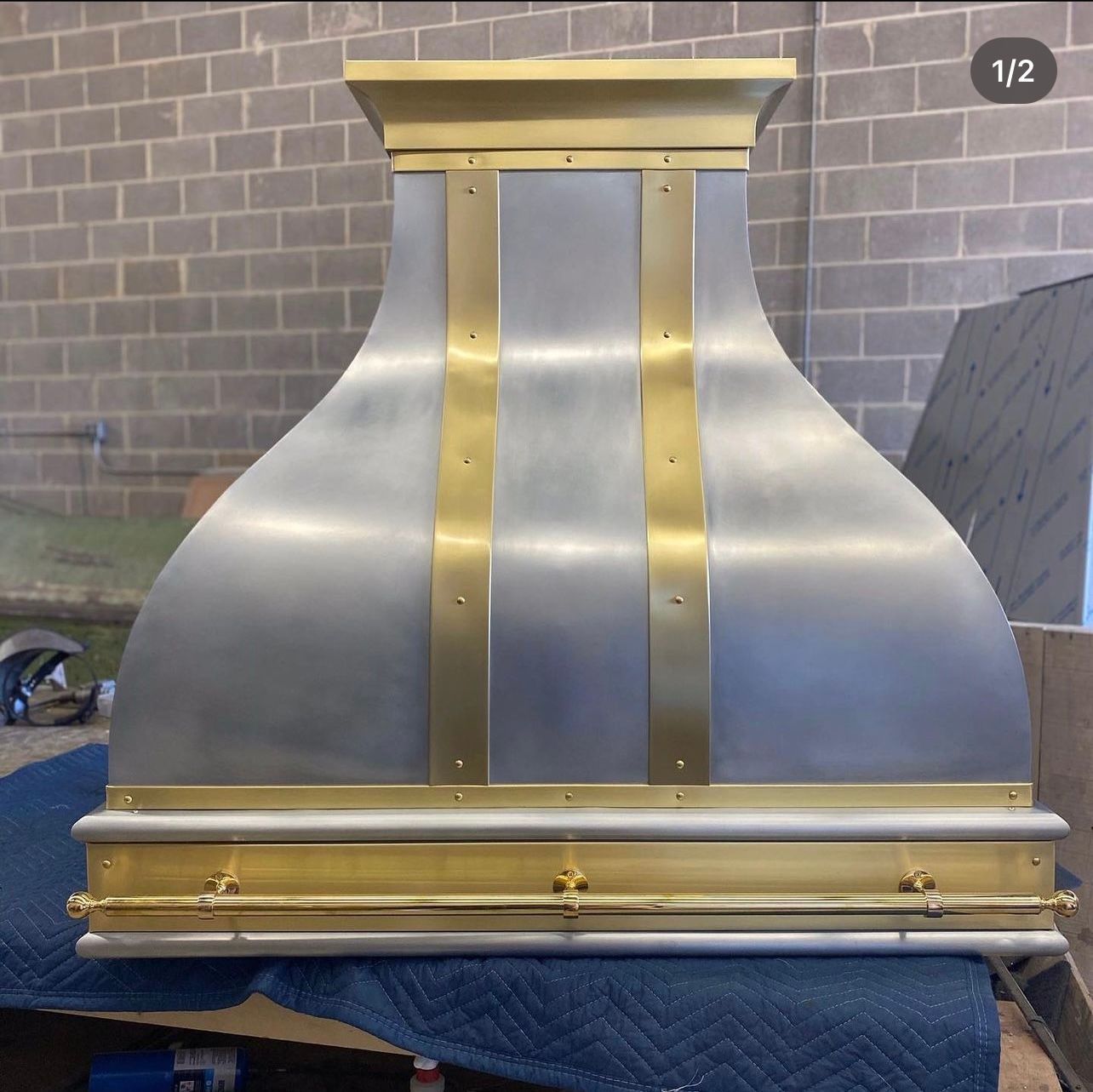 Metallic gold and silver chimney hood on a workbench in front of a brick wall