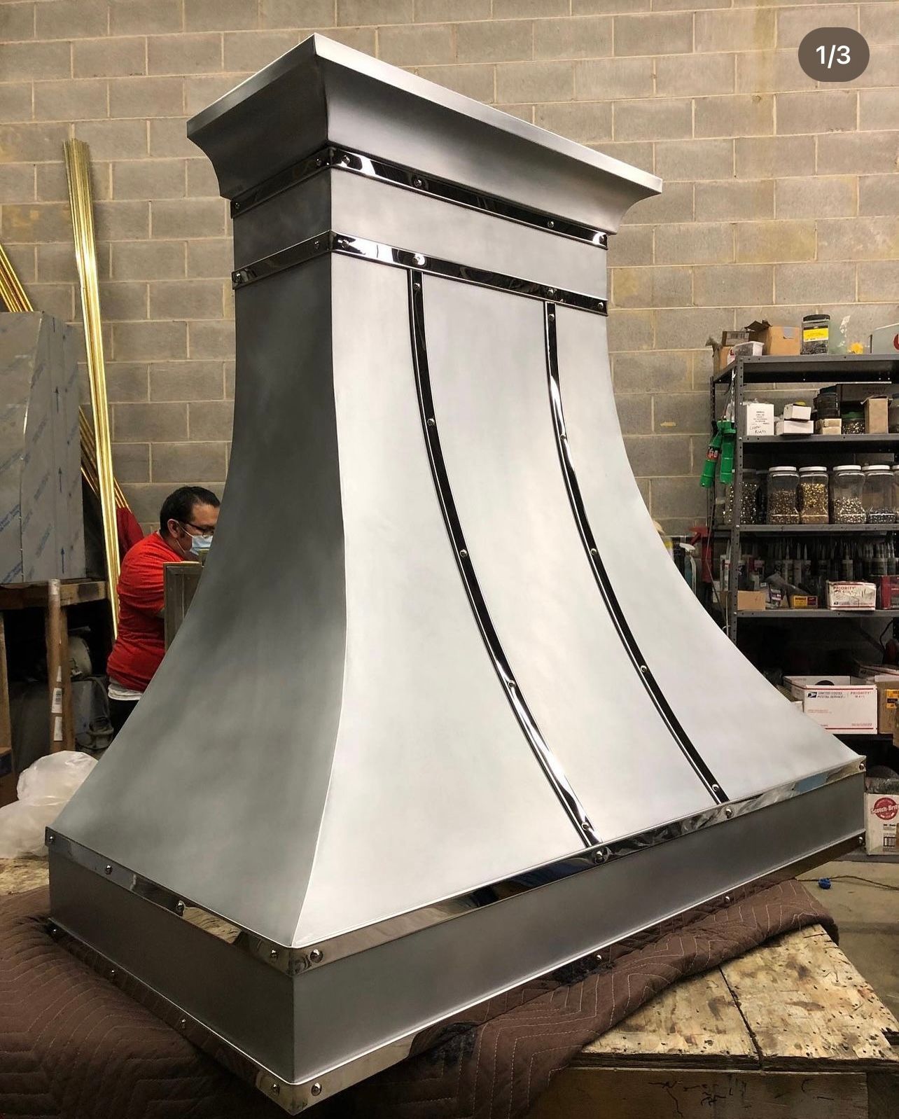 Large silver metal ventilation hood in a workshop, with black trim and a square top base.
