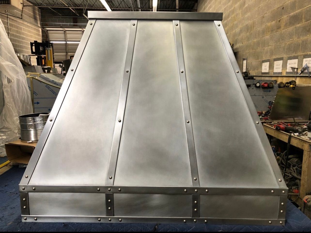 Large stainless steel industrial machine or vent hood in a workshop, viewed from the front