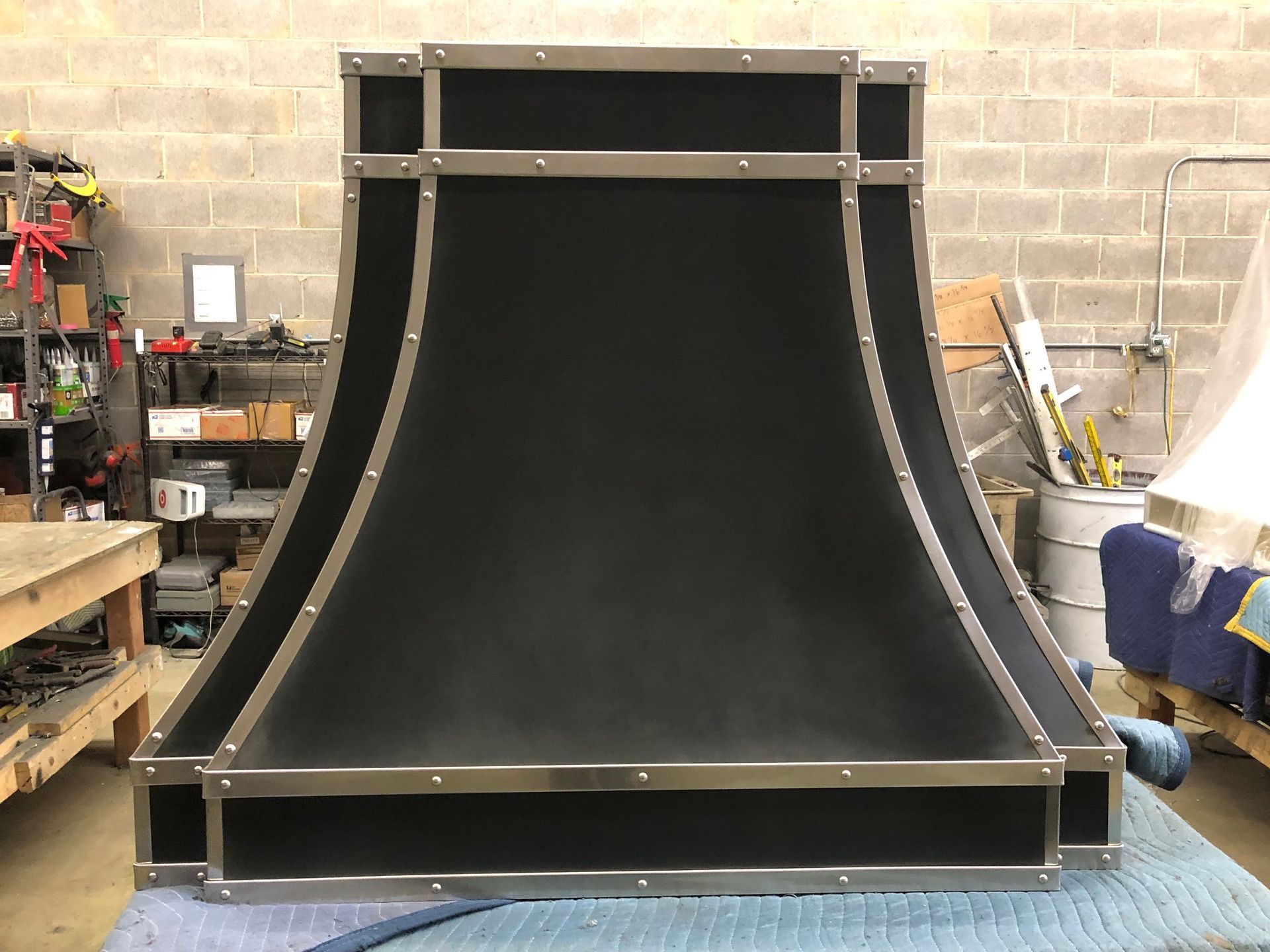Black mini half-pipe ramp in a workshop, with metal framing and shelves in the background