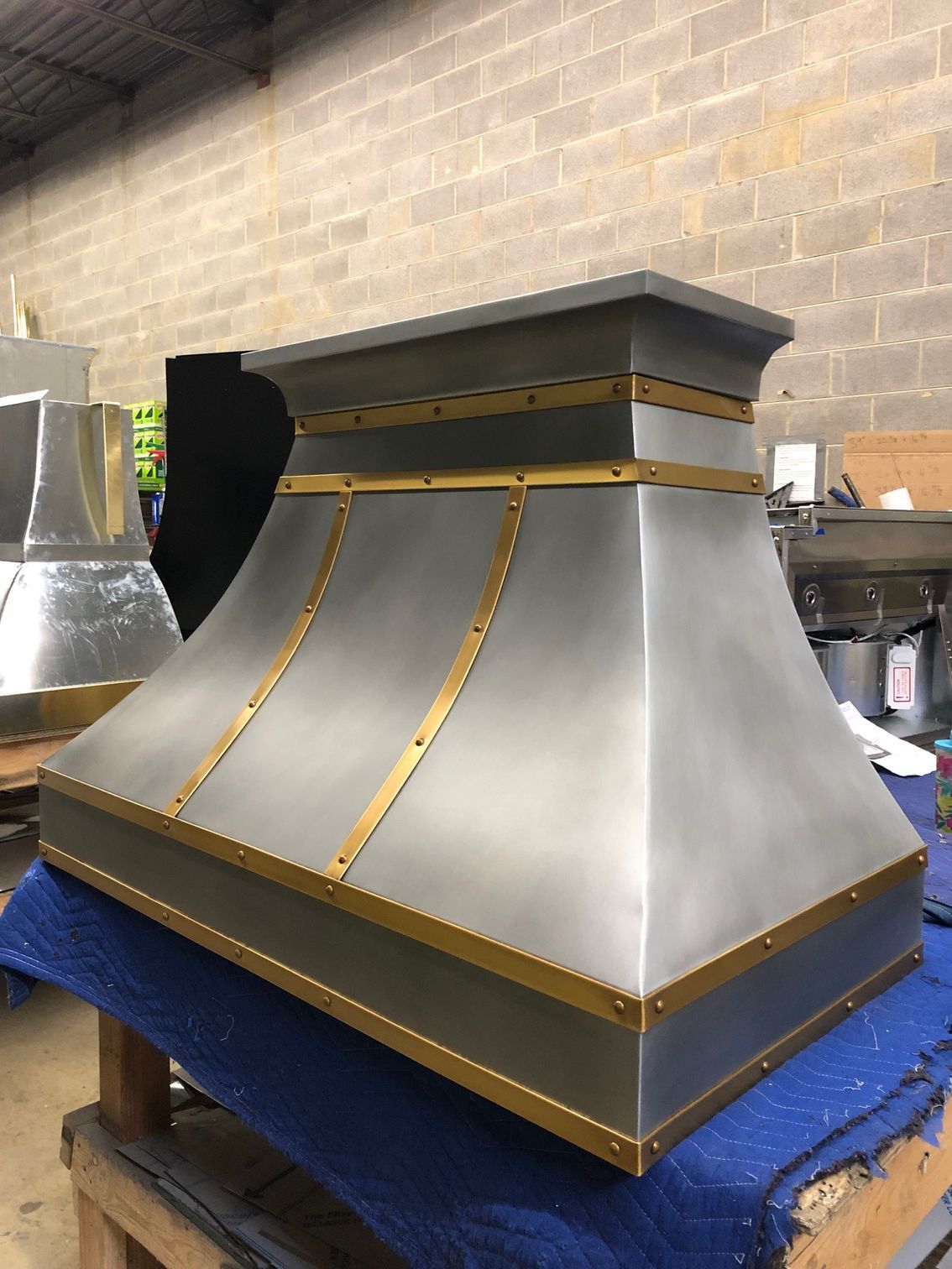 Stainless steel industrial hood with gold trim on a blue workbench in a workshop