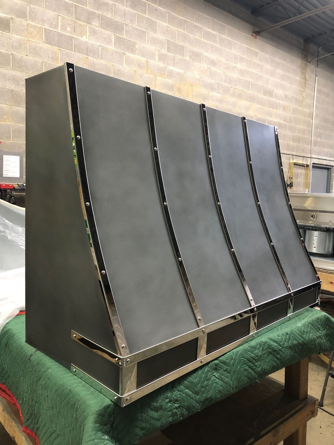 Large black industrial panel with curved ribs, leaning on a workbench in a warehouse or workshop.