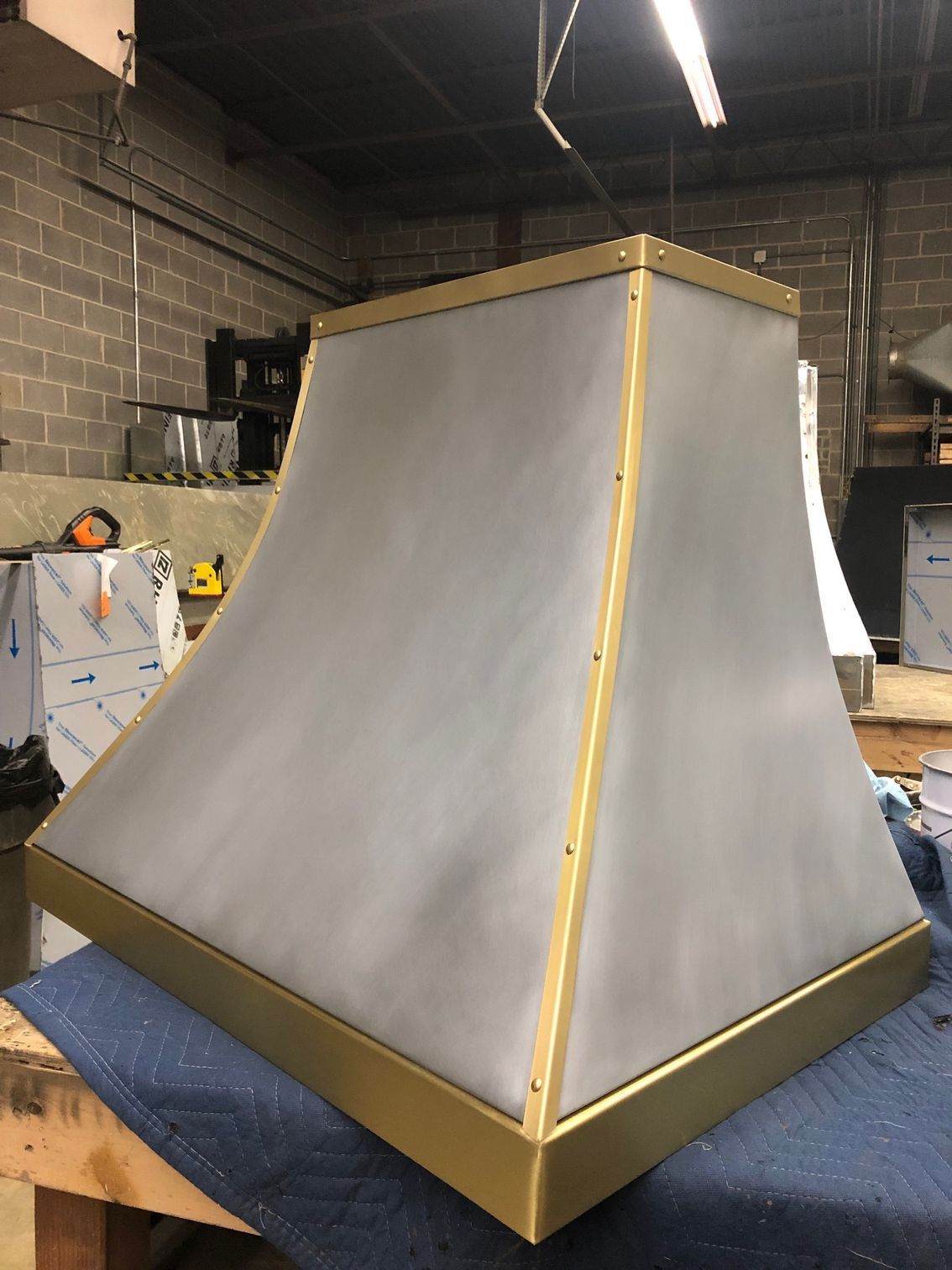 Large gray tapered metal hood with gold trim in a workshop on a workbench