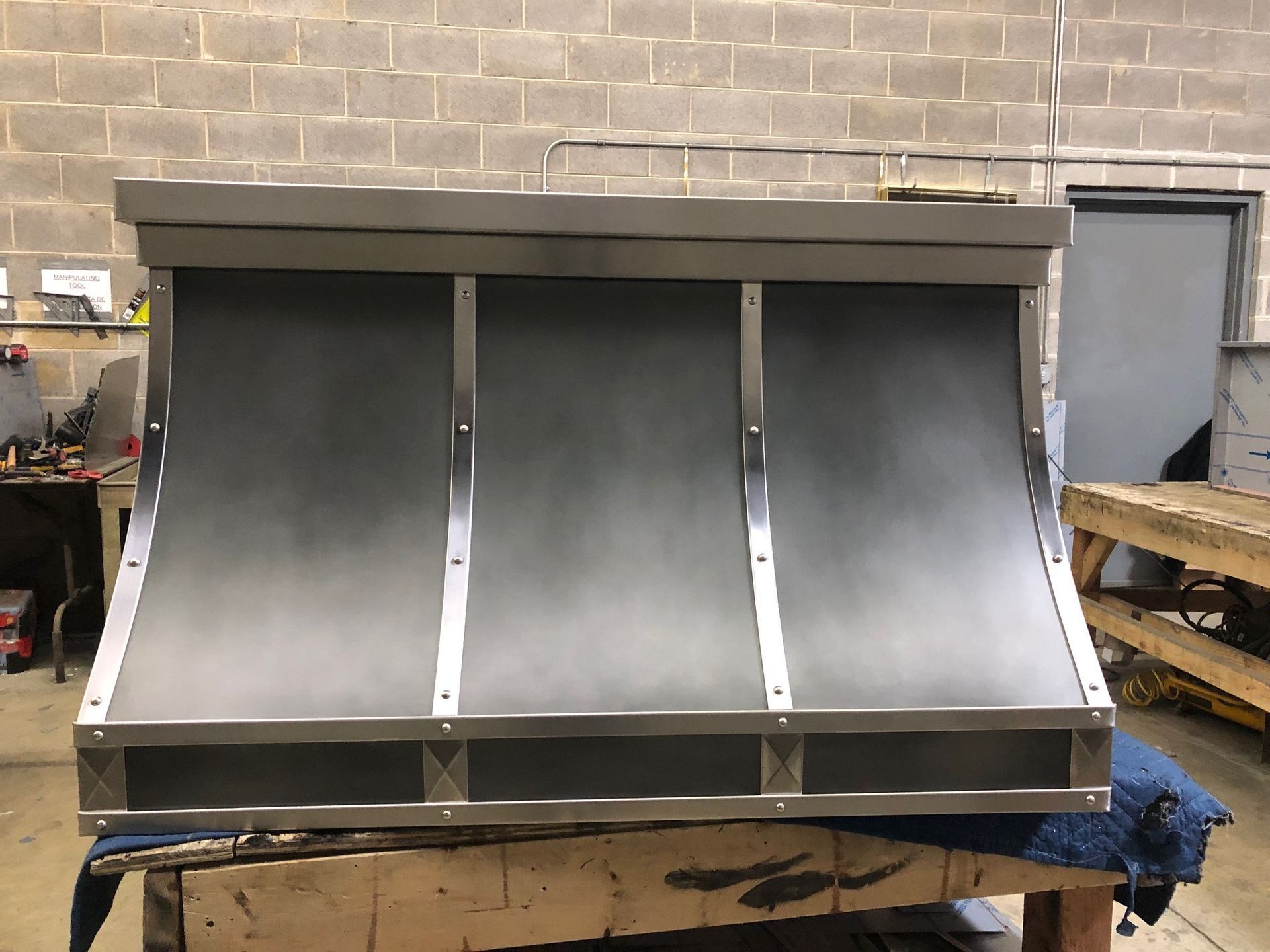 Large stainless steel three-bay sink or wash station against a brick wall in a workshop.