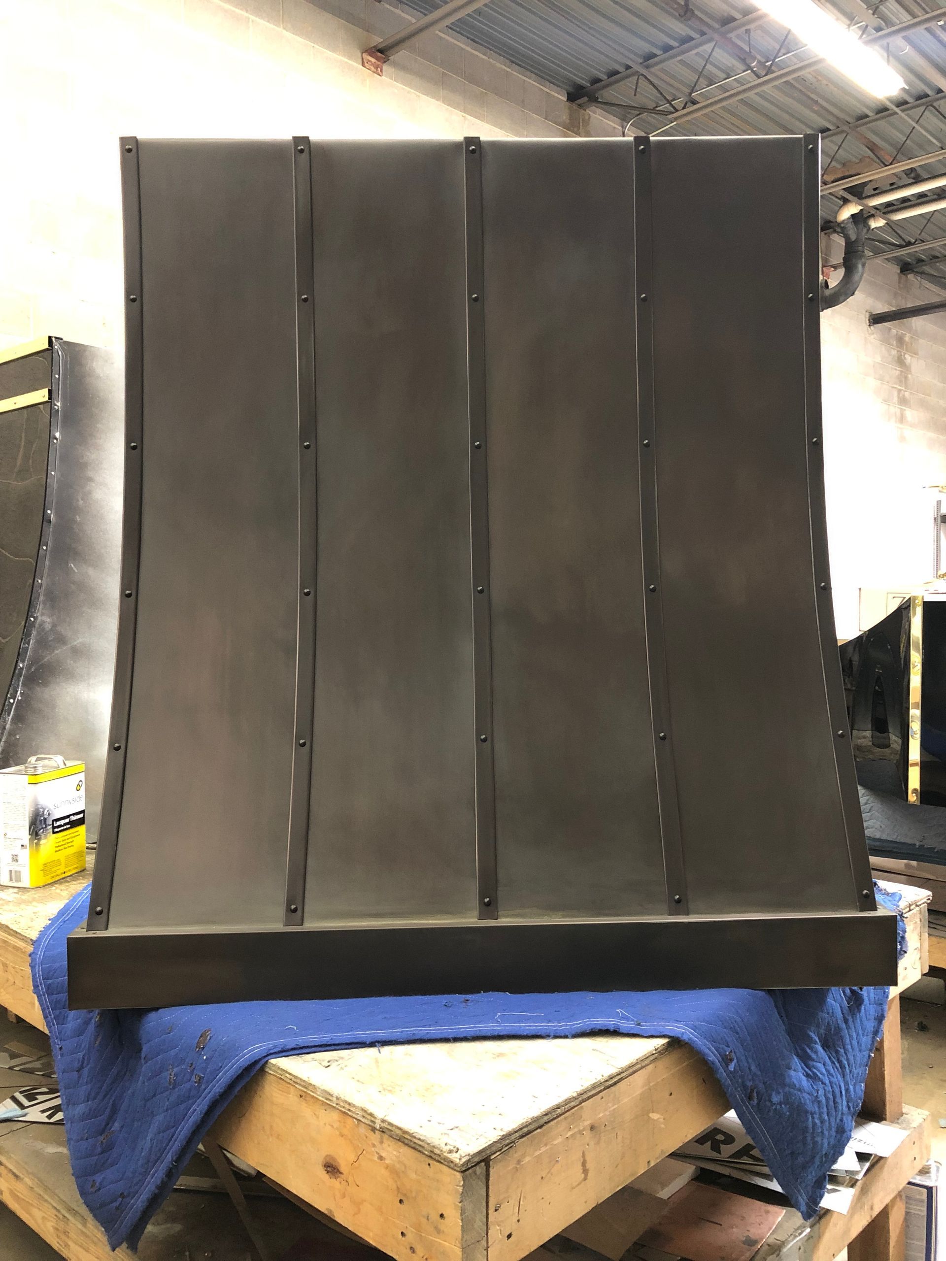 Large black padded panel standing on a workbench in a workshop, draped with a blue cloth.