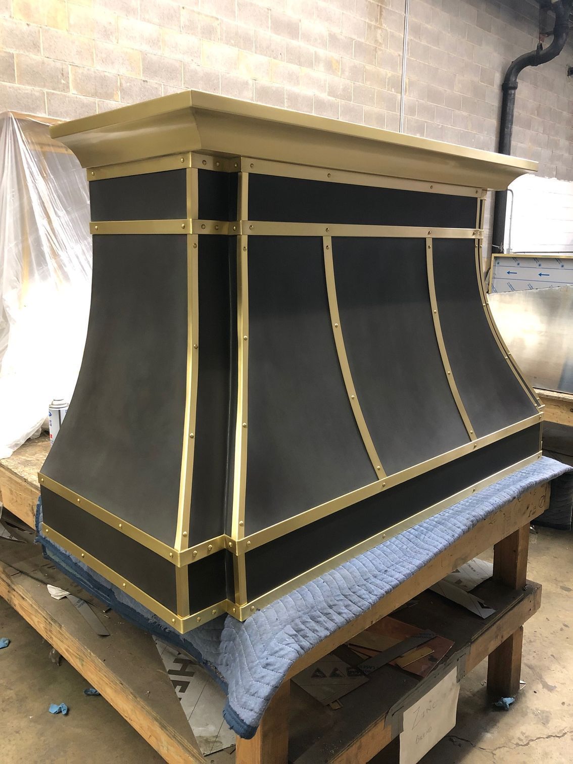 Large black-and-gold decorative structure on a workbench in a workshop, partly covered with protective cloth