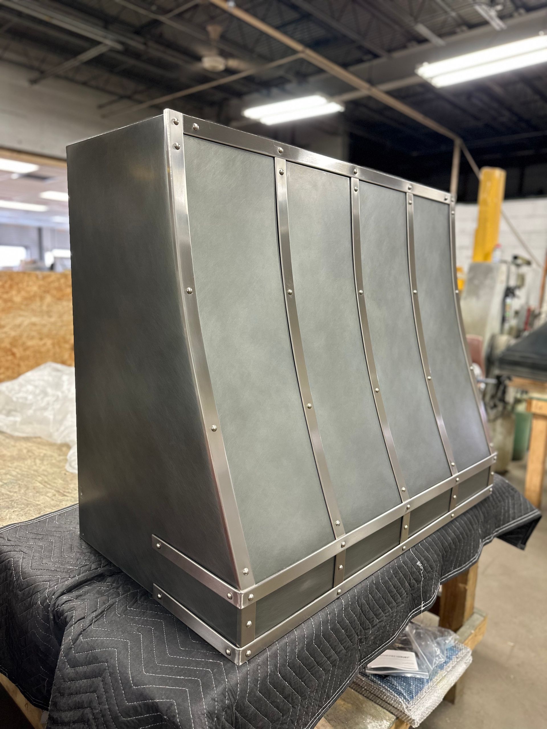 Large metal industrial hood with curved panels on a factory floor