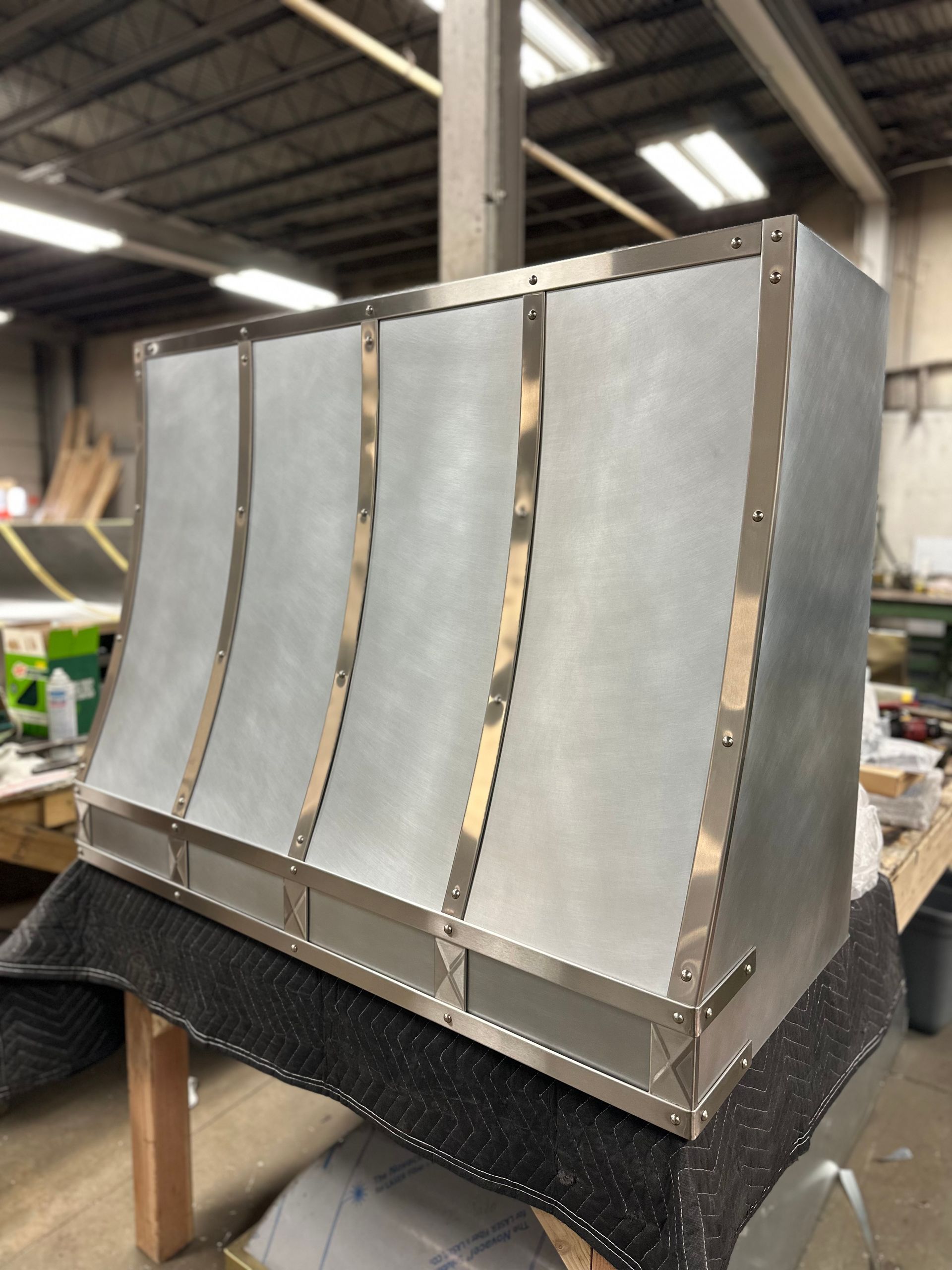 Metal prototype with four curved silver panels on a workbench in an industrial workshop