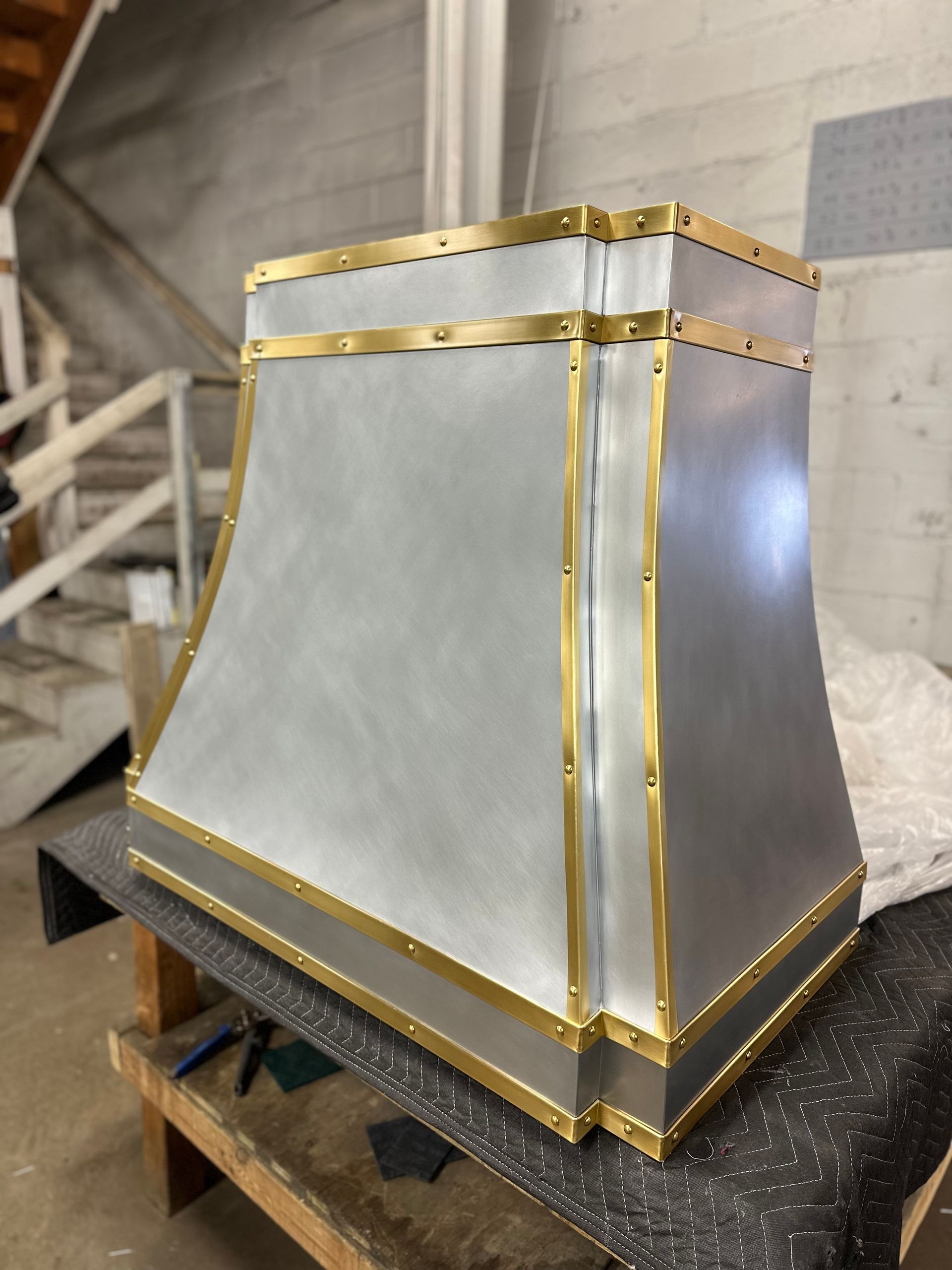 Metallic silver and gold decorative hood or chimney cap on a wooden pallet in a workshop