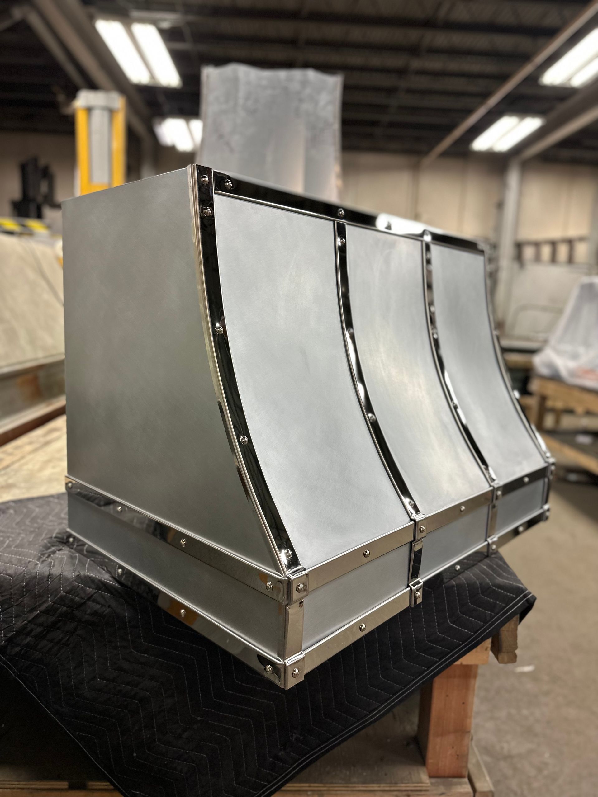 Metal industrial component with curved silver panels and black trim on a workshop table