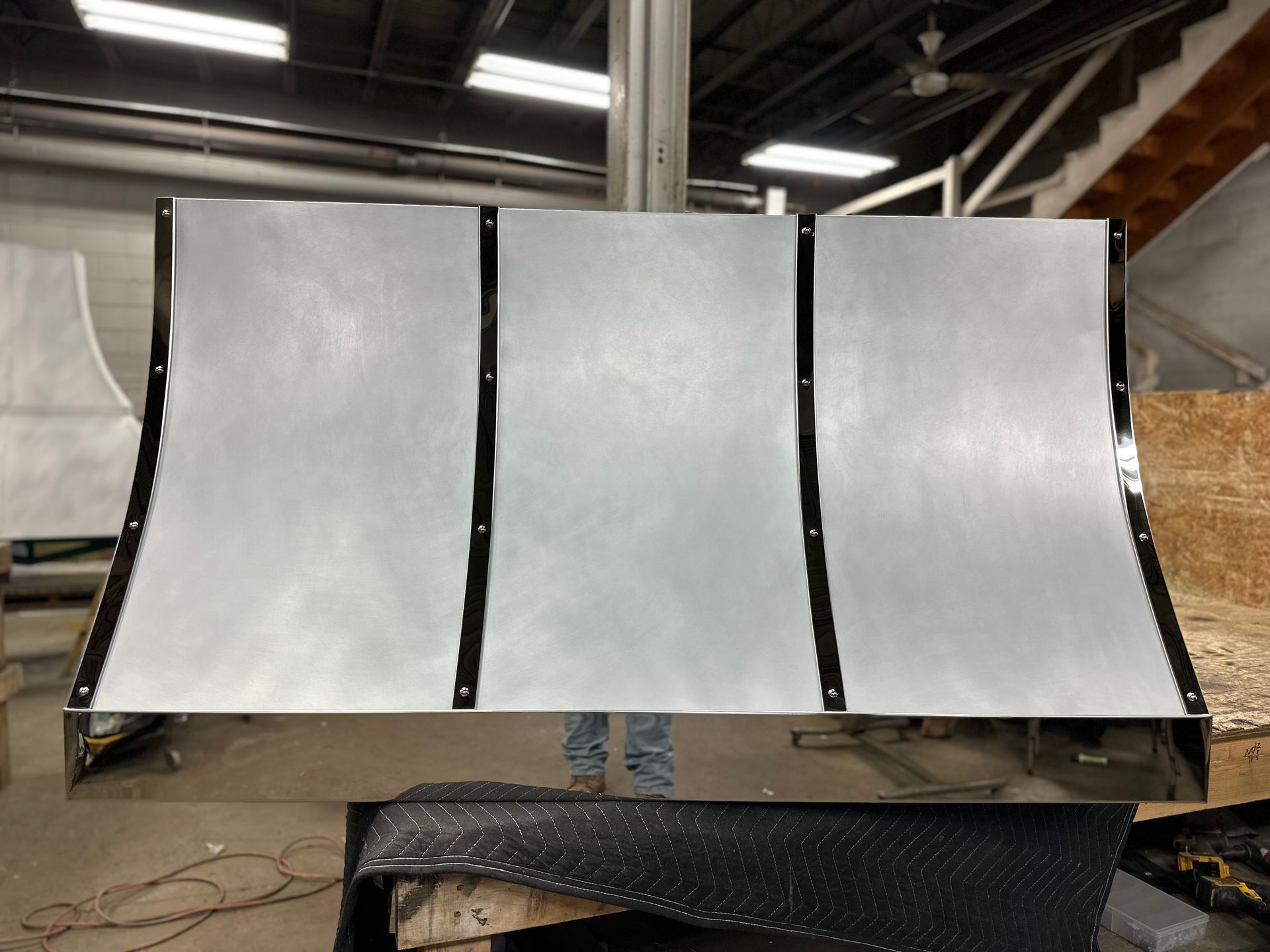Three-panel metallic display screen in an industrial workshop, with white panels and black frames.
