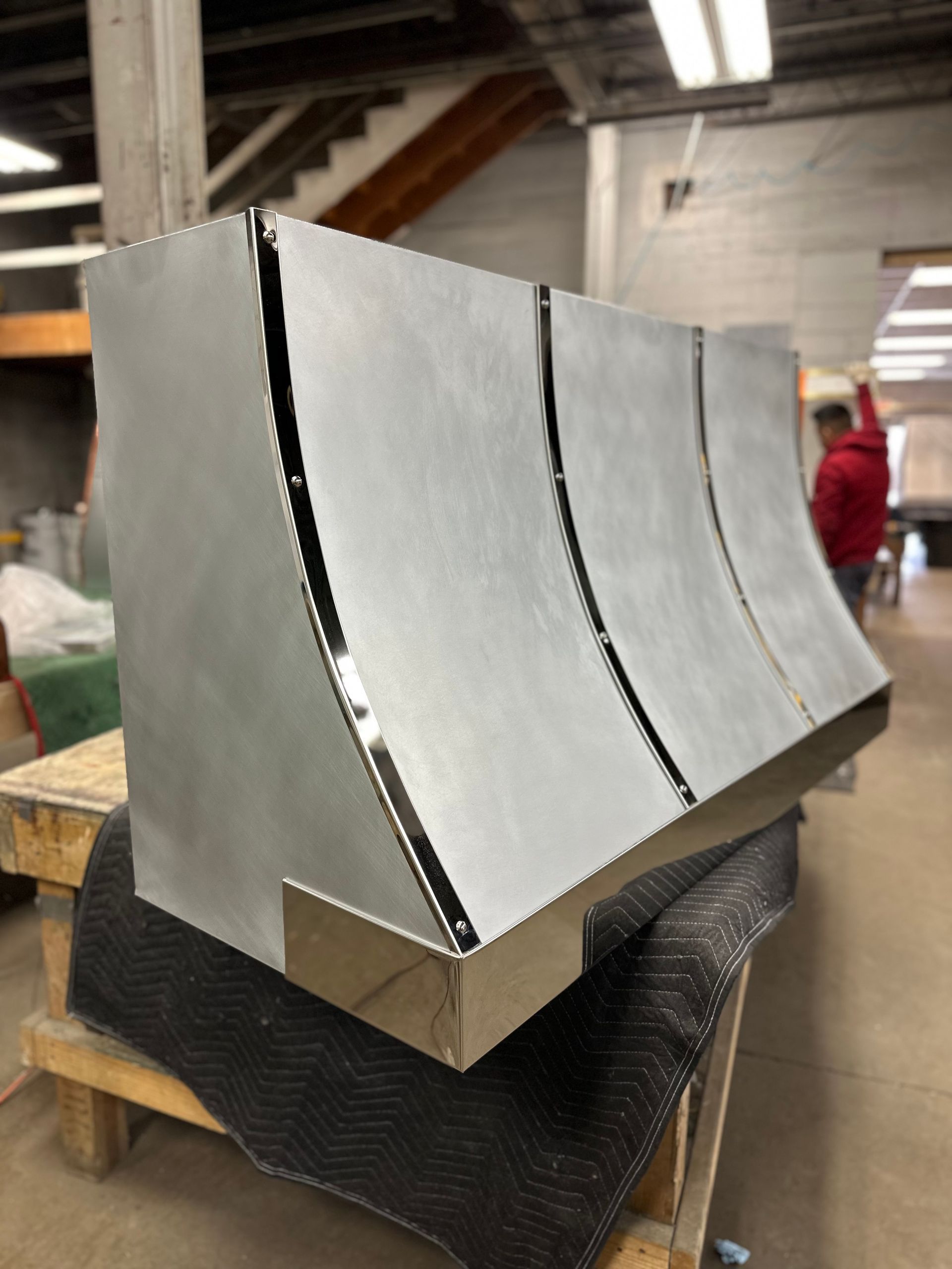 Large silver metal panel with curved vertical grooves, leaning on a pallet in an industrial workshop.