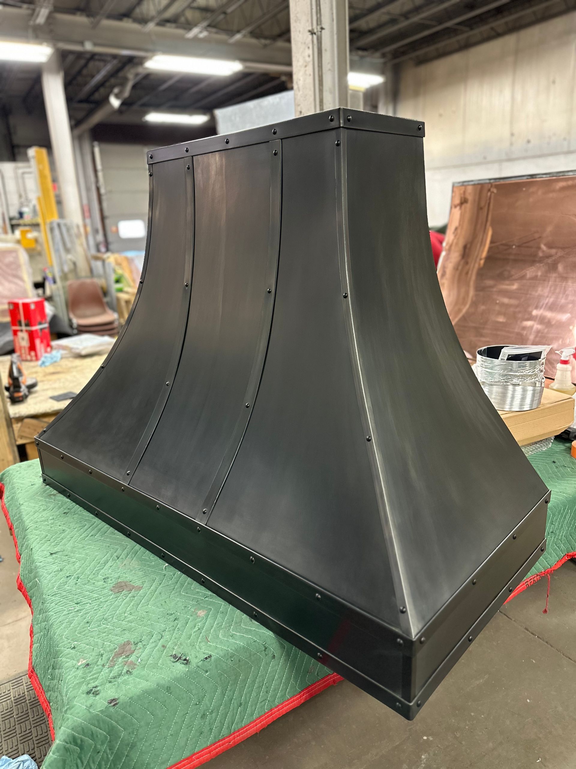 Black metal ventilation hood in an industrial workshop, with green foam support underneath.