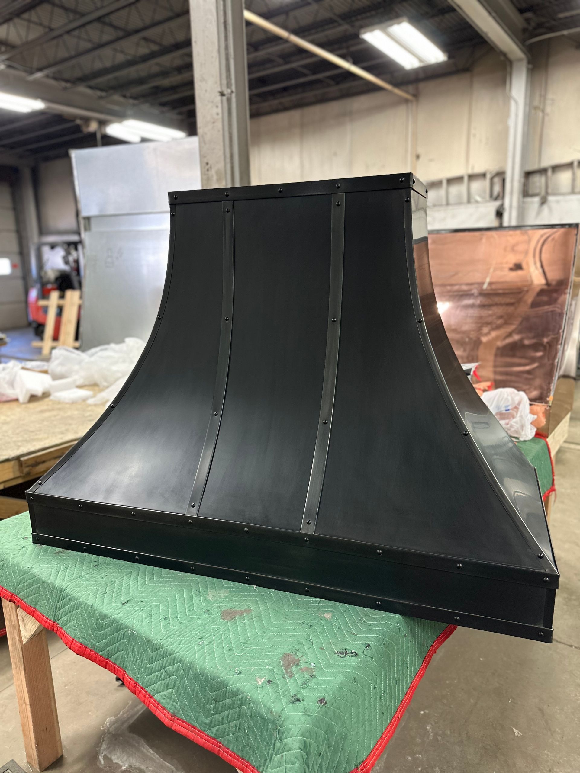 Black metal curved duct on a green workbench in an industrial workshop