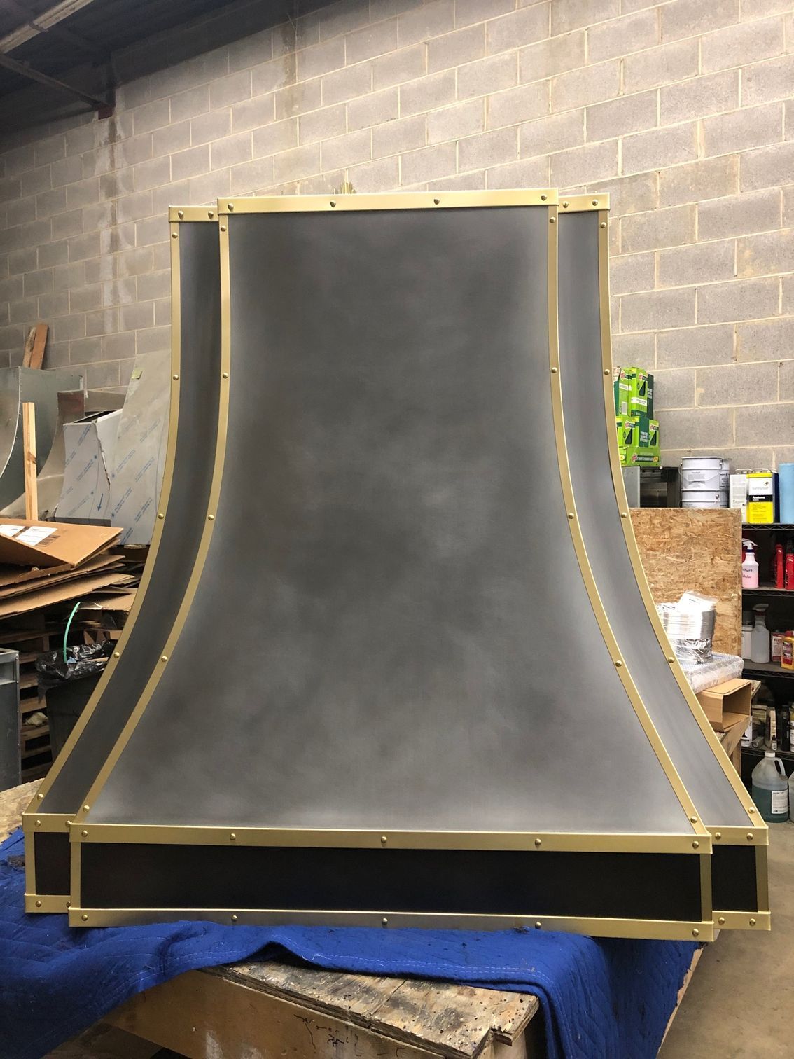 Large black curved wall panel with gold trim, standing on a blue blanket in a workshop.